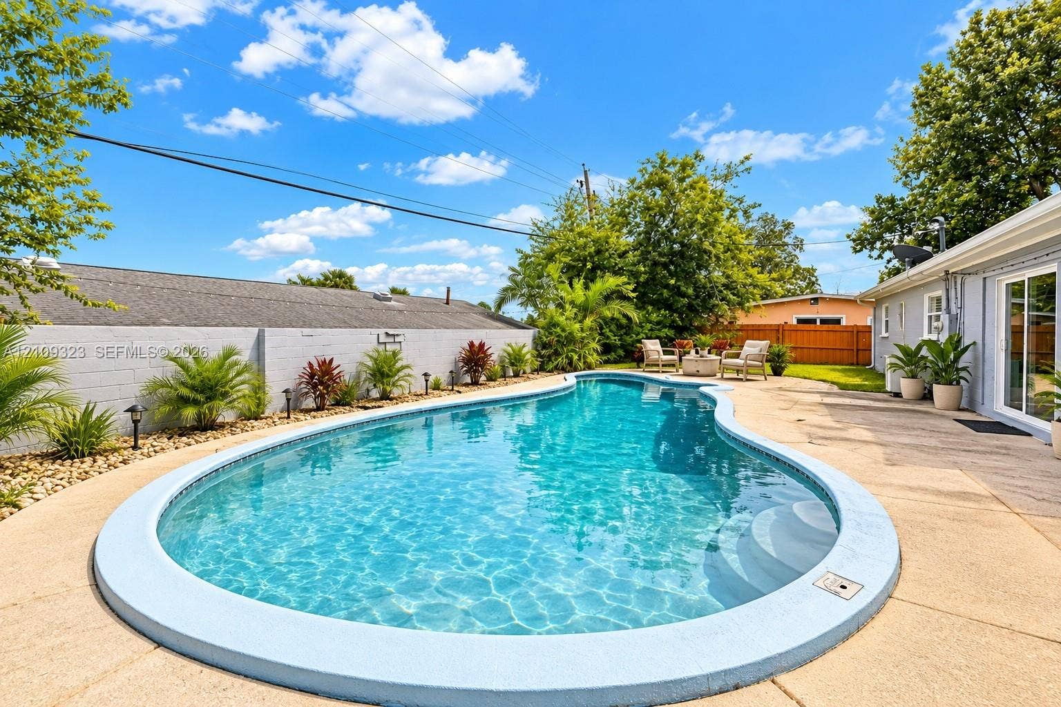 911 Shady Park Terrace, Daytona Beach, FL 32117 Curved swimming pool featuring a concrete deck, perimeter landscaping, and a masonry privacy wall