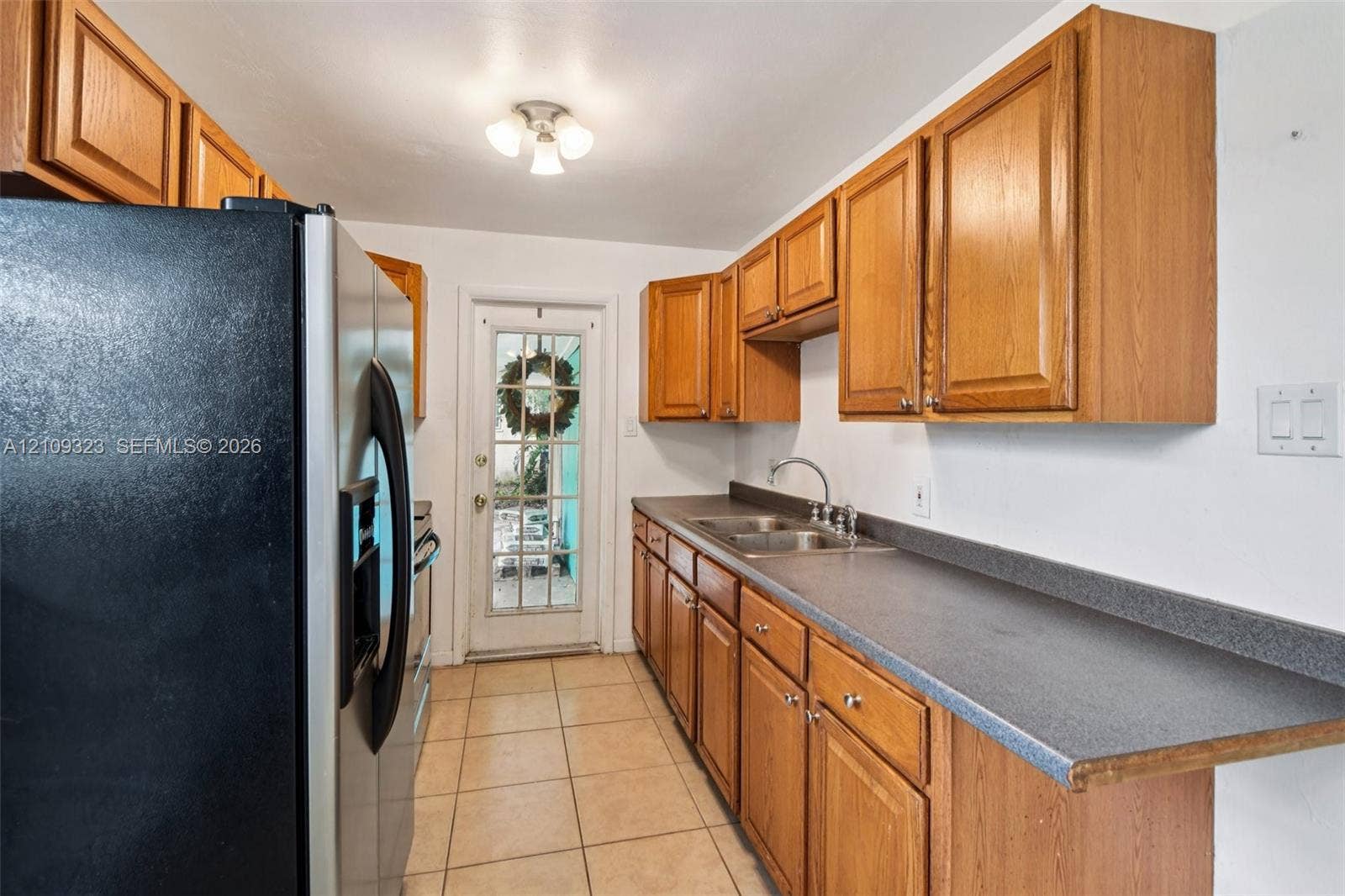 911 Shady Park Terrace, Daytona Beach, FL 32117 Kitchen featuring wood cabinetry, solid-surface countertops, stainless steel refrigerator, dual-basin sink with faucet, and tile flooring