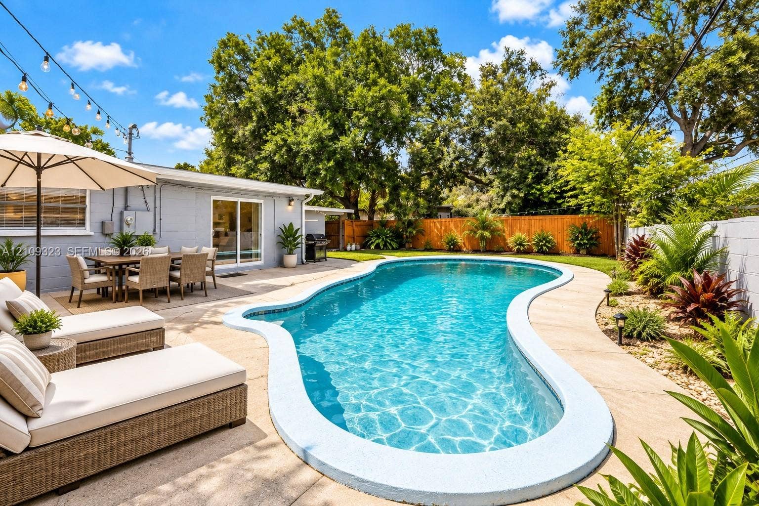 911 Shady Park Terrace, Daytona Beach, FL 32117 Backyard featuring a freeform swimming pool, expansive concrete decking, mature trees, and privacy fencing