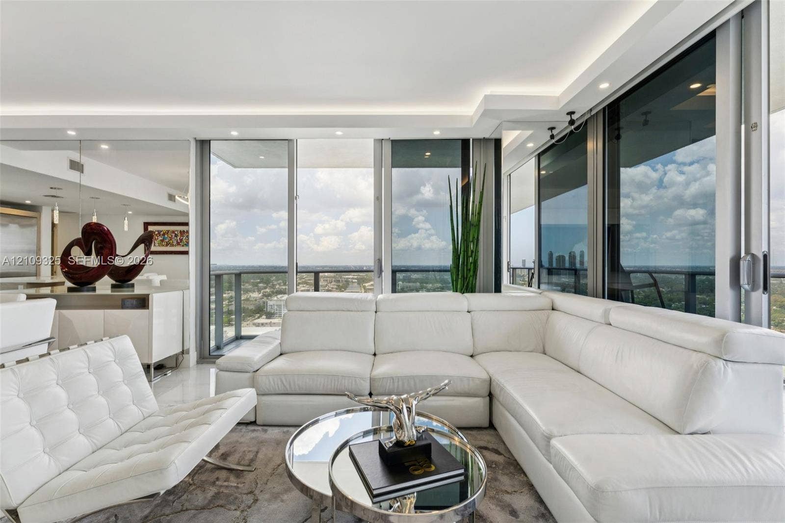 Floor-to-ceiling sliding glass doors, recessed ceiling lighting, polished stone flooring, and expansive exterior balcony access