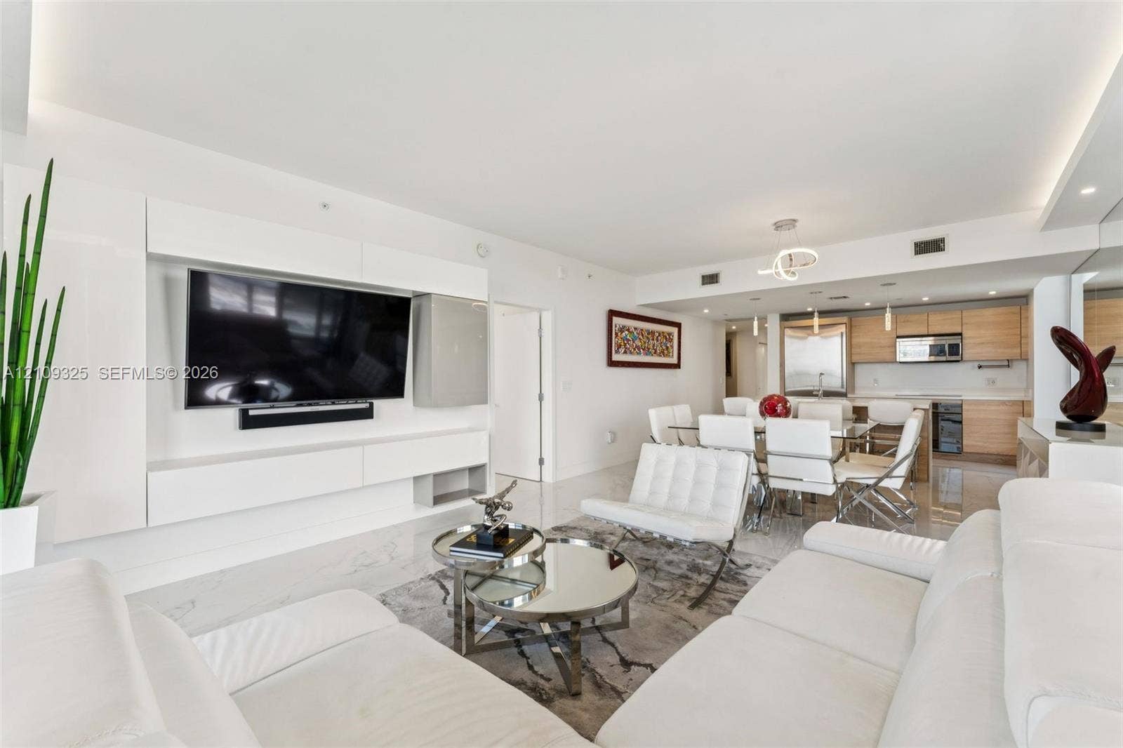 Open-concept interior featuring large-format tile flooring, recessed ceiling lighting, a custom built-in white media console, and a kitchen equipped with light wood-finish cabinetry