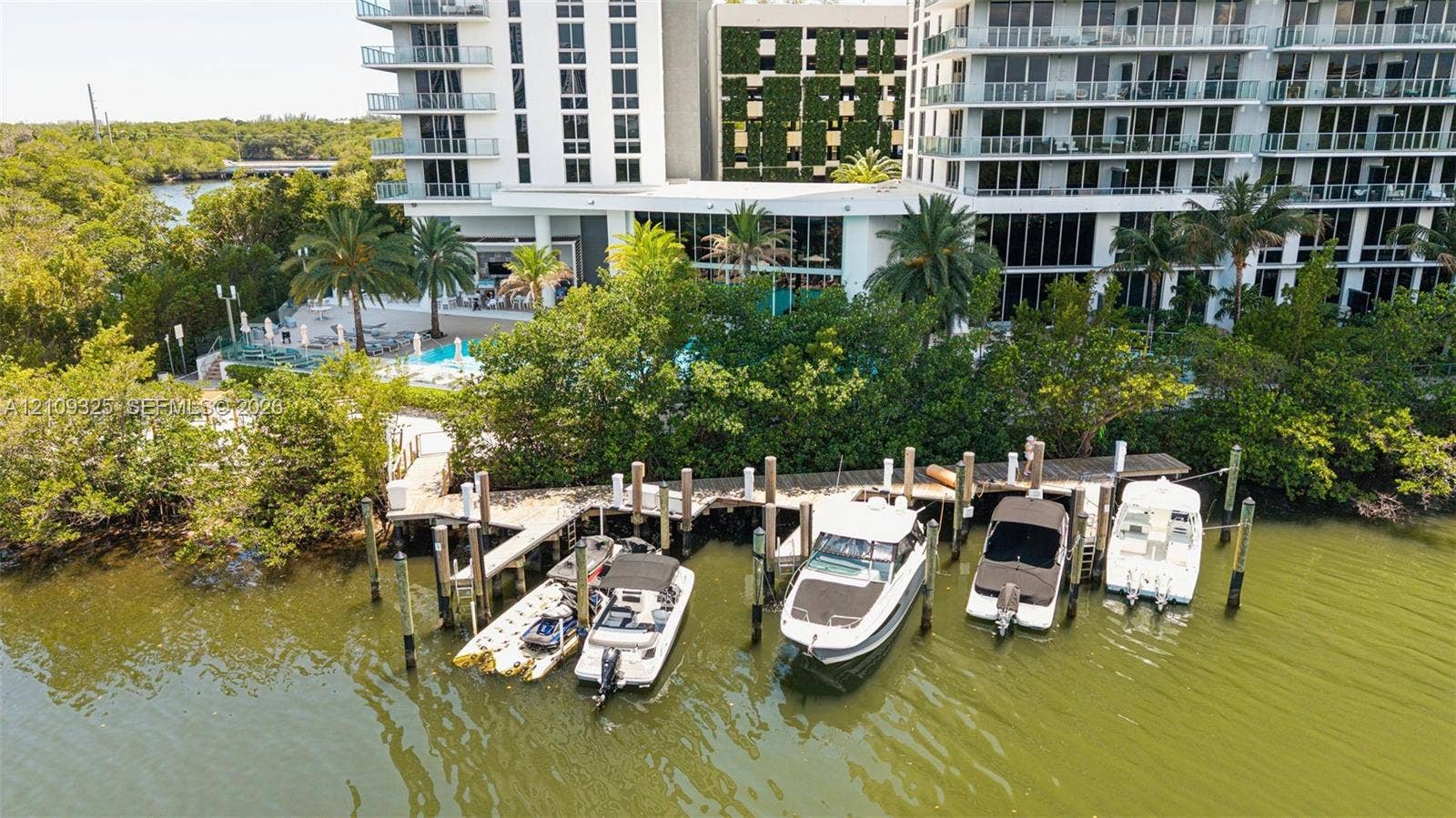 Deep-water dock with multiple boat slips, swimming pool, palm-lined landscaping, and multi-story structural exterior