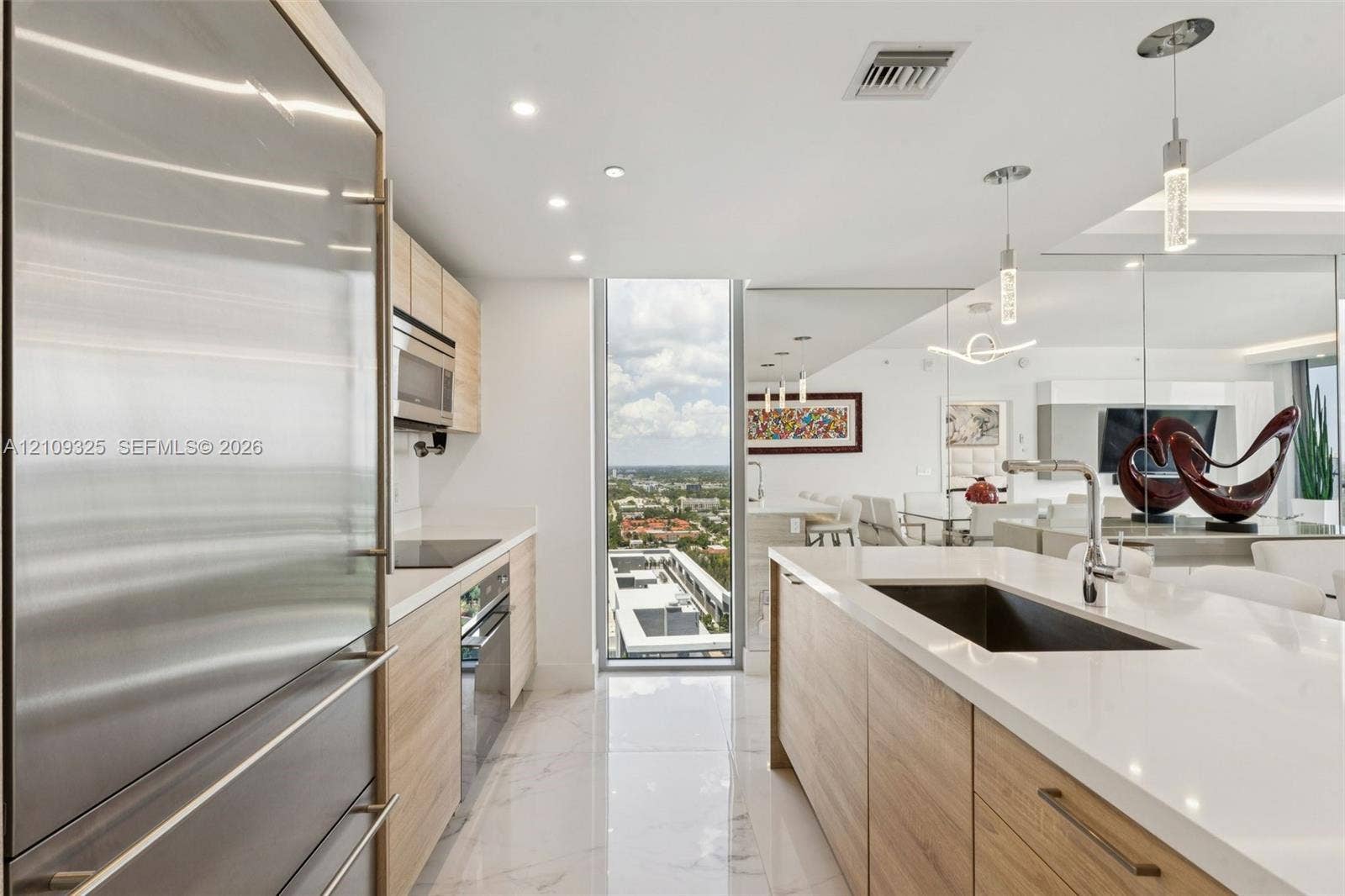 Kitchen featuring custom wood-finish cabinetry, white stone countertops, stainless steel appliances, a center island with an integrated sink, and polished porcelain flooring