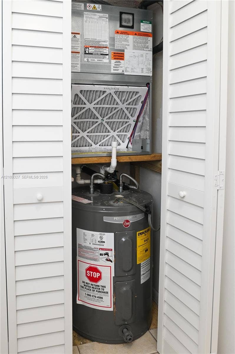 Utility closet featuring white bi-fold doors, a vertical air handler unit, and a tank-style water heater