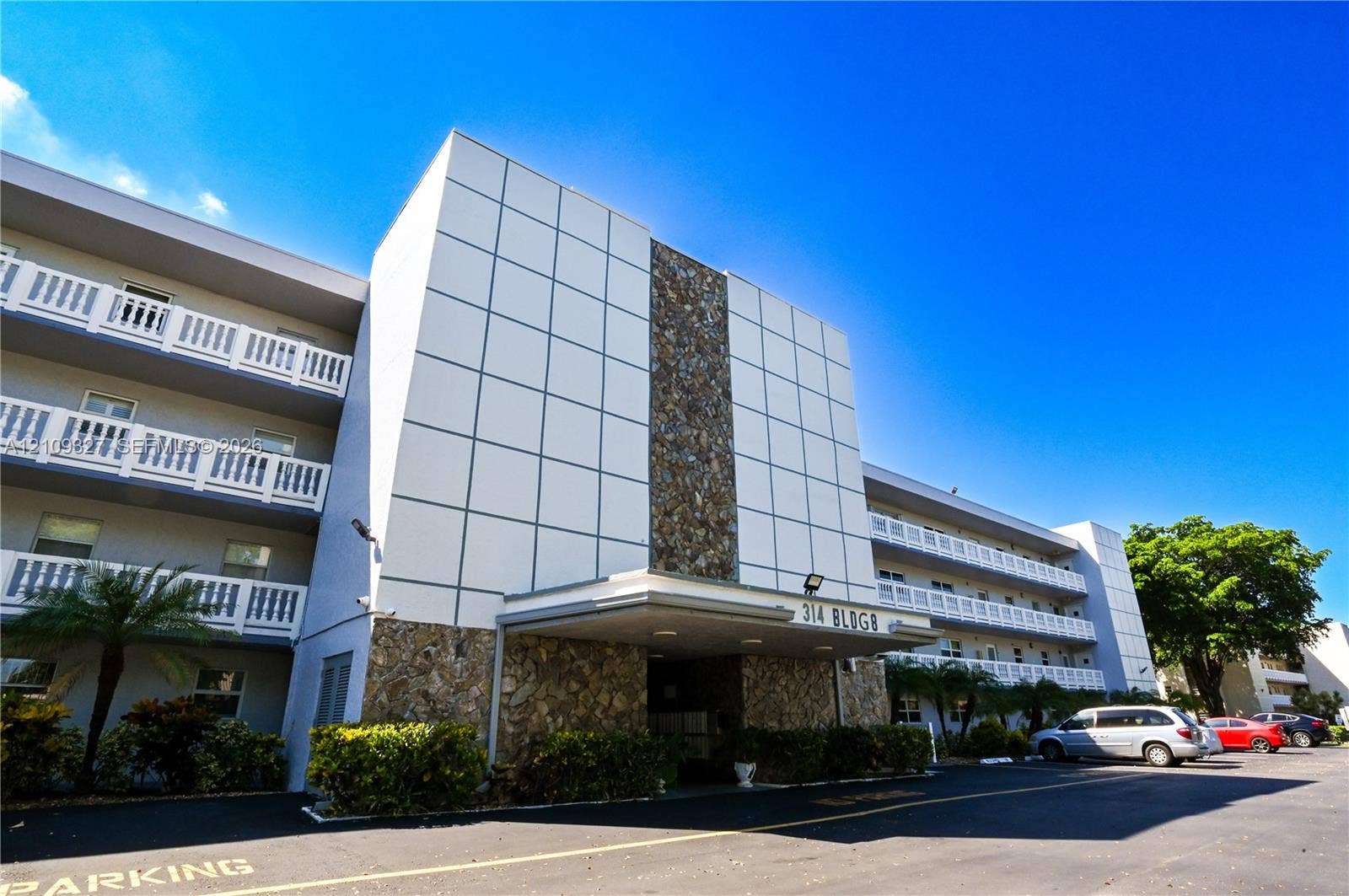Mid-rise building exterior featuring a panelized faade, stone masonry detailing, a covered entrance, and tiered private balconies with white railings