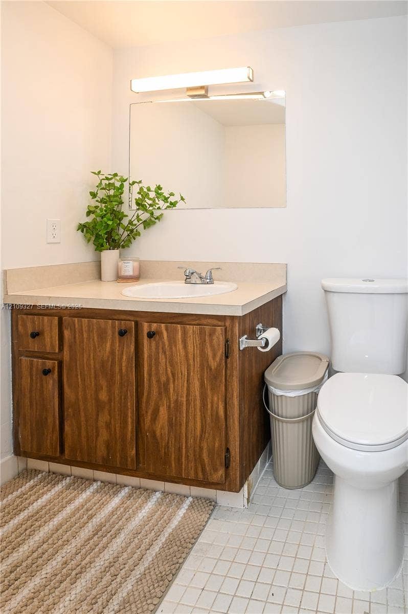 Bathroom featuring a wood-finish vanity cabinet, light-toned solid surface countertop, integrated oval sink, frameless wall-mounted mirror, and linear light fixture