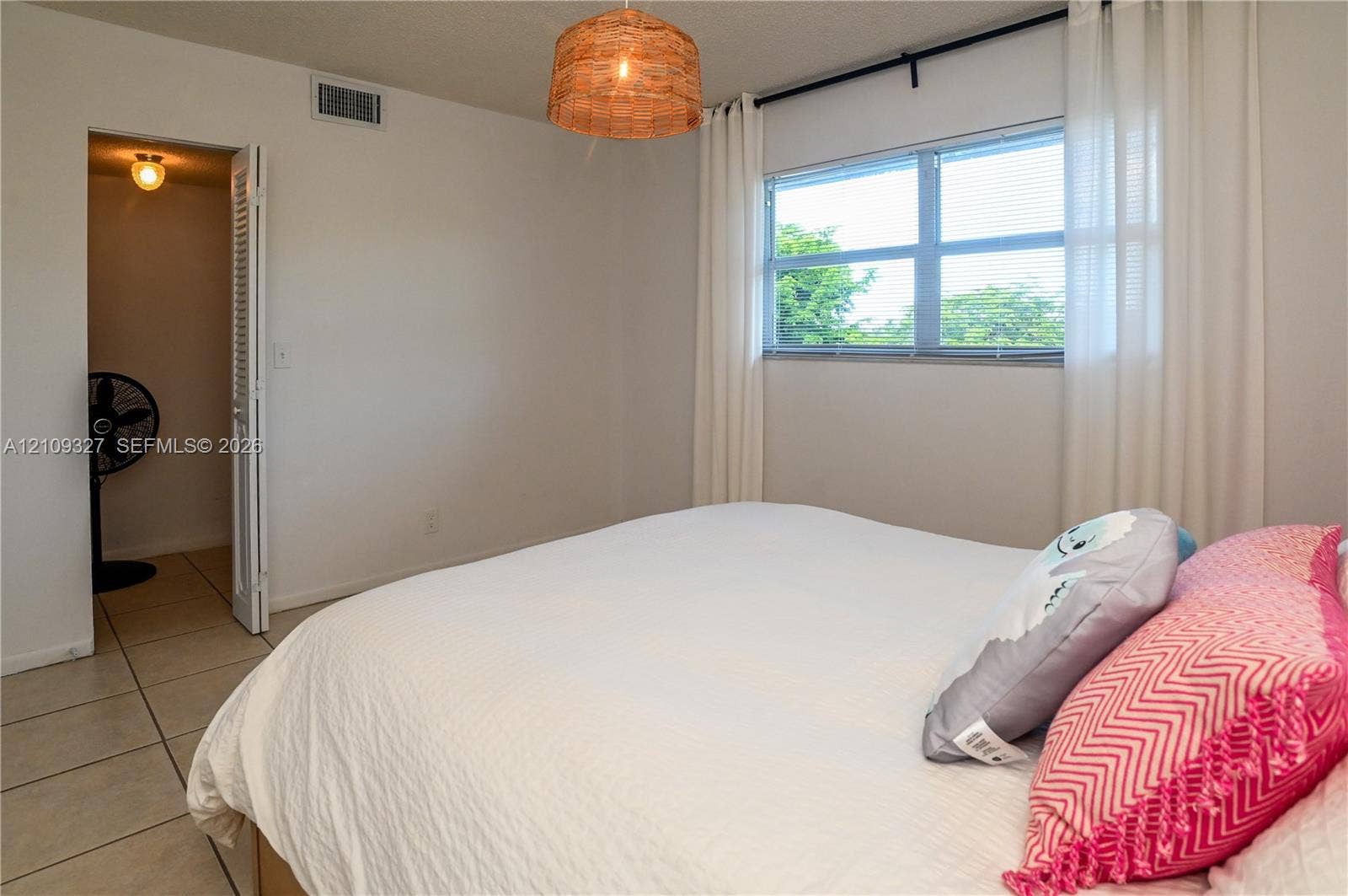 Neutral-toned room featuring ceramic tile flooring, a large window, a woven-texture hanging light fixture, and a louvered-door closet