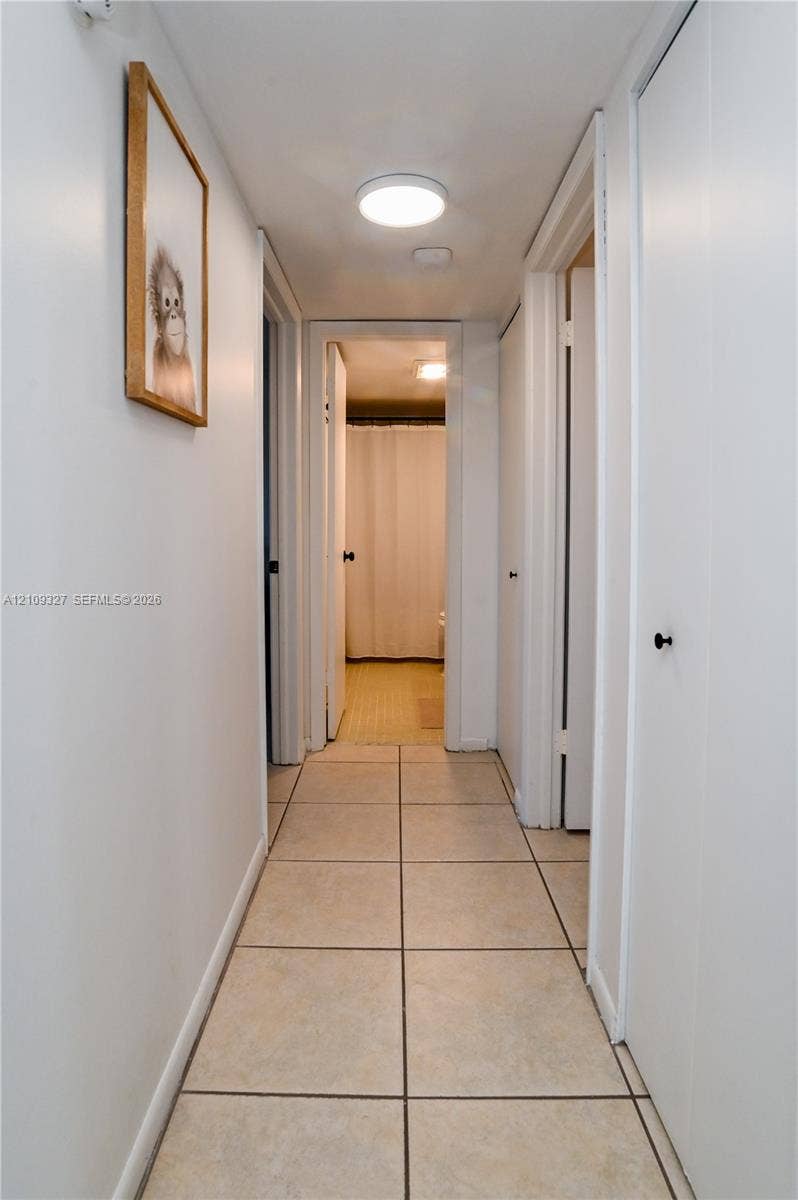 Hallway featuring neutral-toned tile flooring, flush-mount lighting, and multiple interior doors