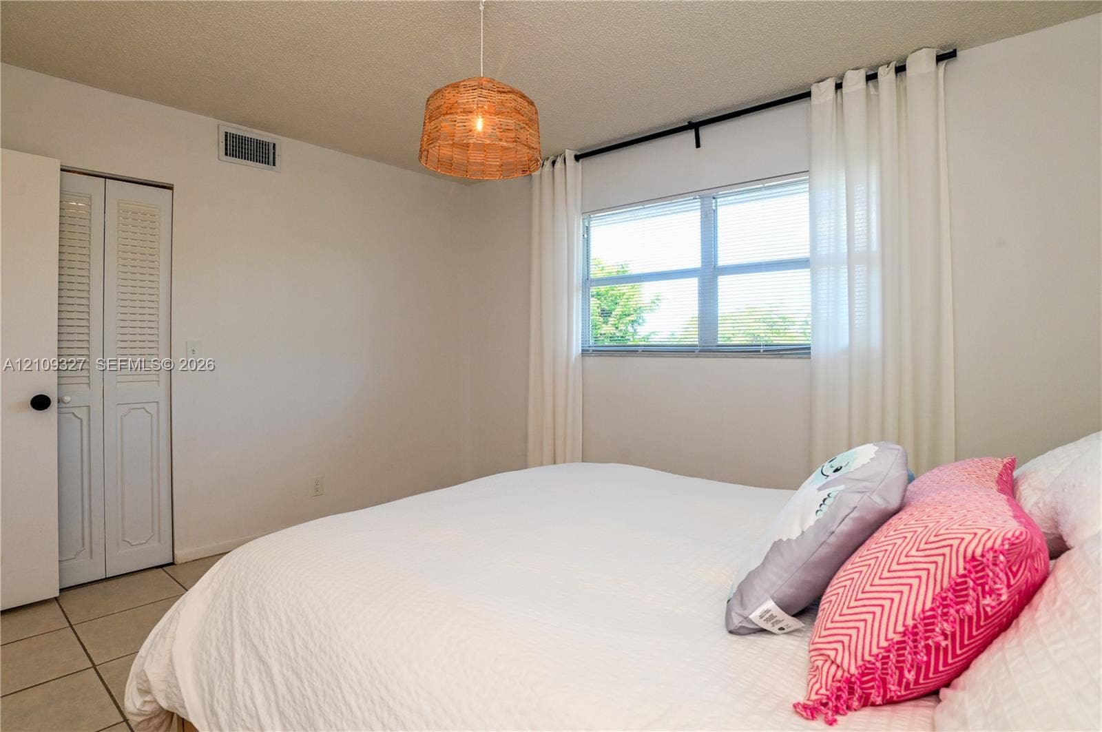 Room featuring light-toned tile flooring, louvered bi-fold closet doors, a window, and a woven pendant light fixture