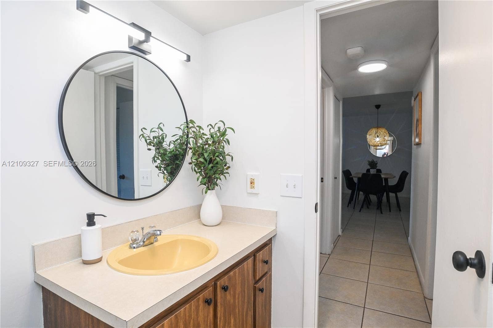 Vanity featuring wood-finish cabinetry, a neutral countertop, an integrated sink, and a circular wall-mounted mirror with integrated lighting