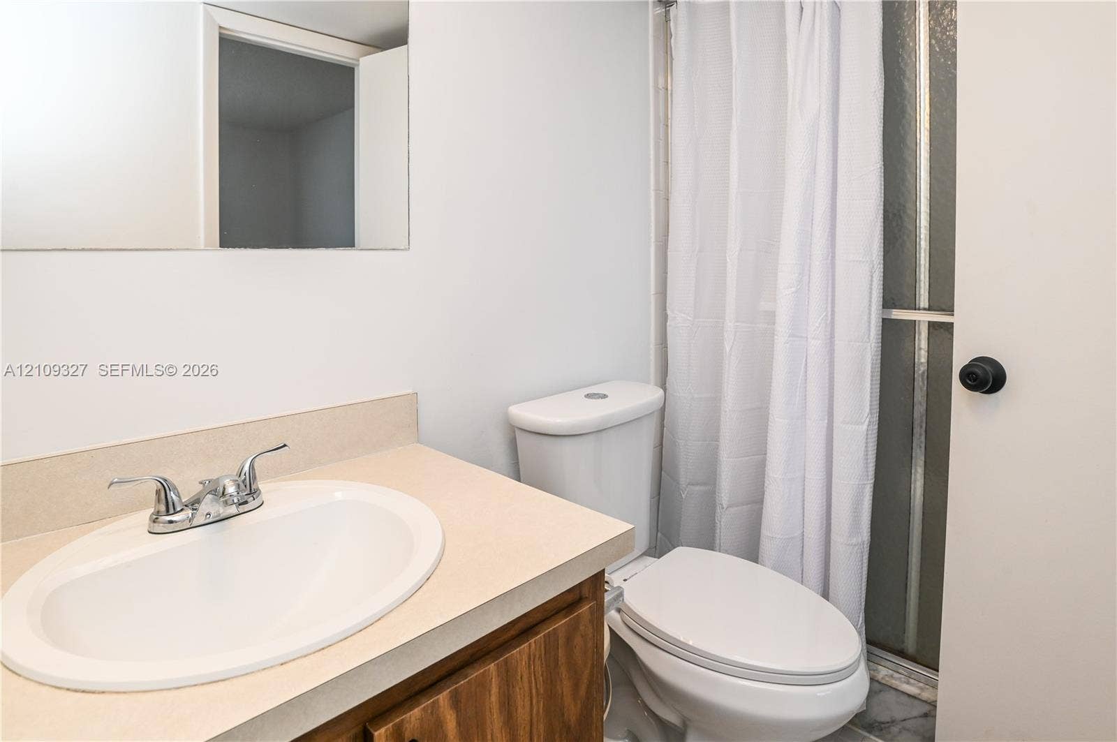 Bathroom featuring a neutral-toned vanity with an integrated basin, dual-handle chrome faucet, wall-mounted mirror, and a walk-in shower enclosure