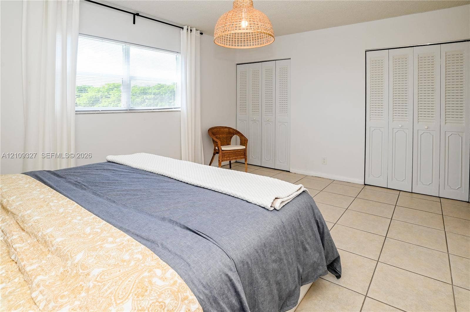 Neutral-toned ceramic tile flooring, sets of white louvered closet doors, and a woven pendant light fixture
