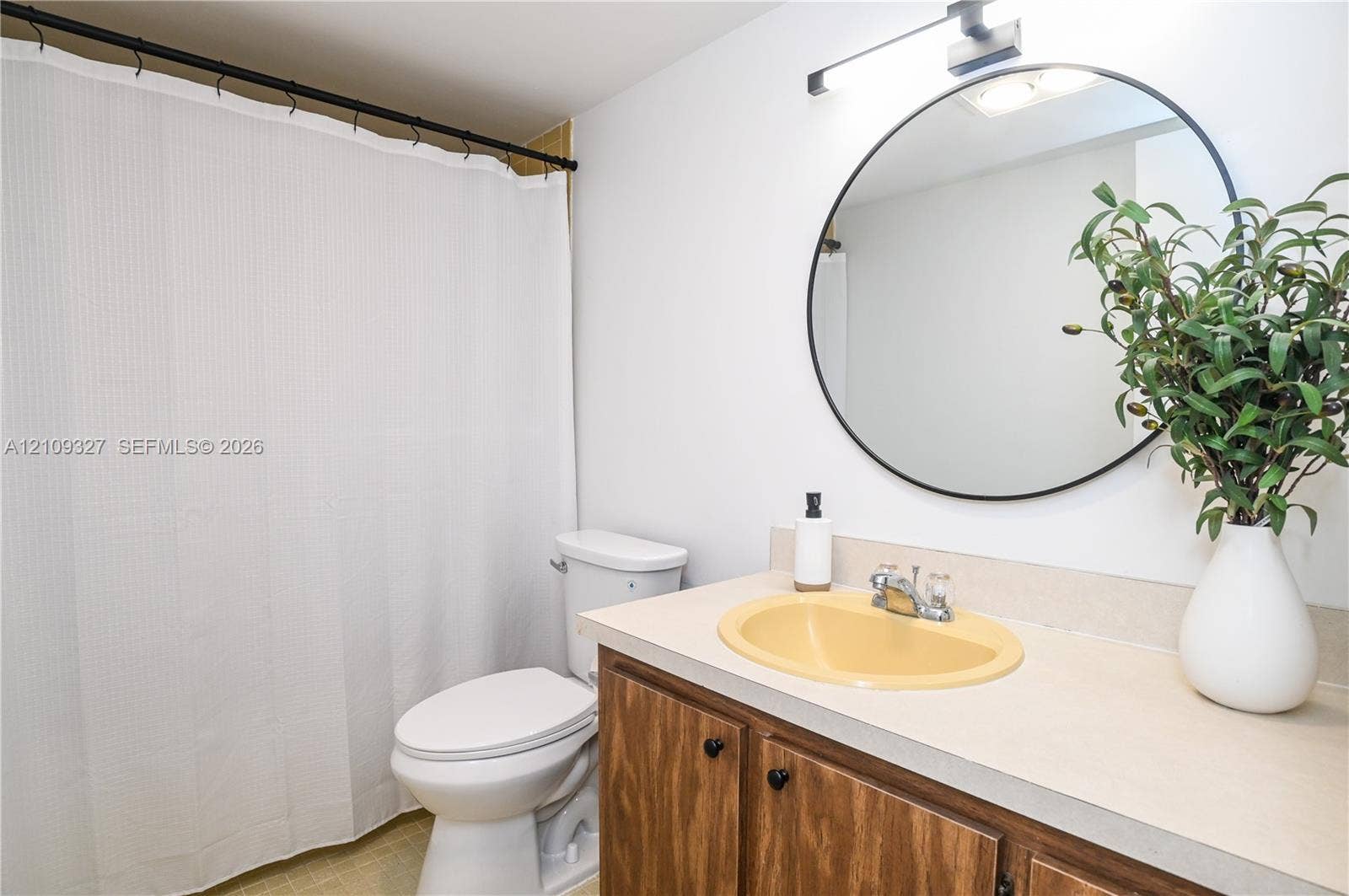 Bathroom featuring a wood-finish vanity with a molded basin, round wall-mounted mirror, and linear light fixture