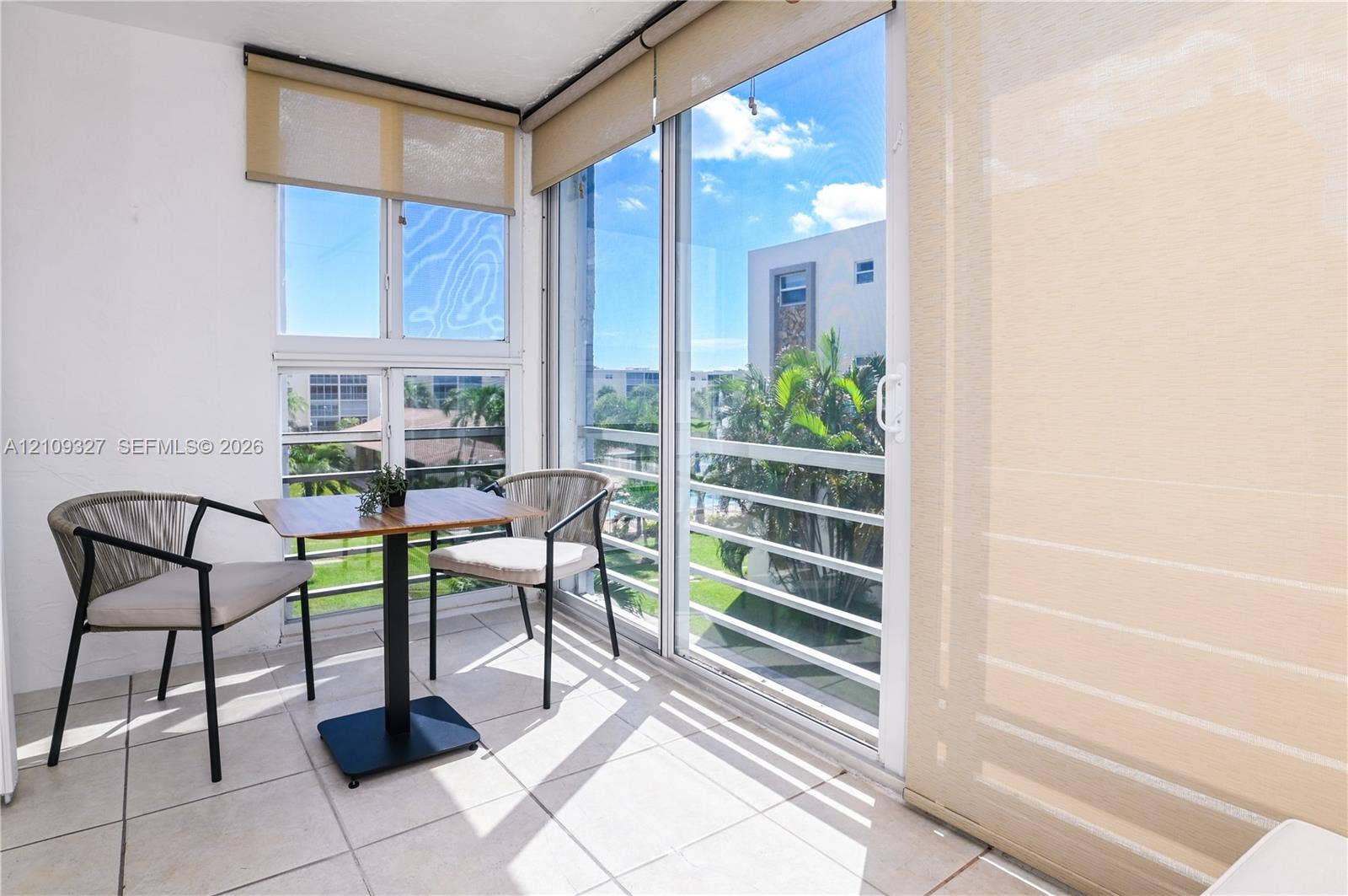Balcony featuring large-format ceramic floor tiles, expansive floor-to-ceiling glass sliding doors, and windows with neutral roller shades