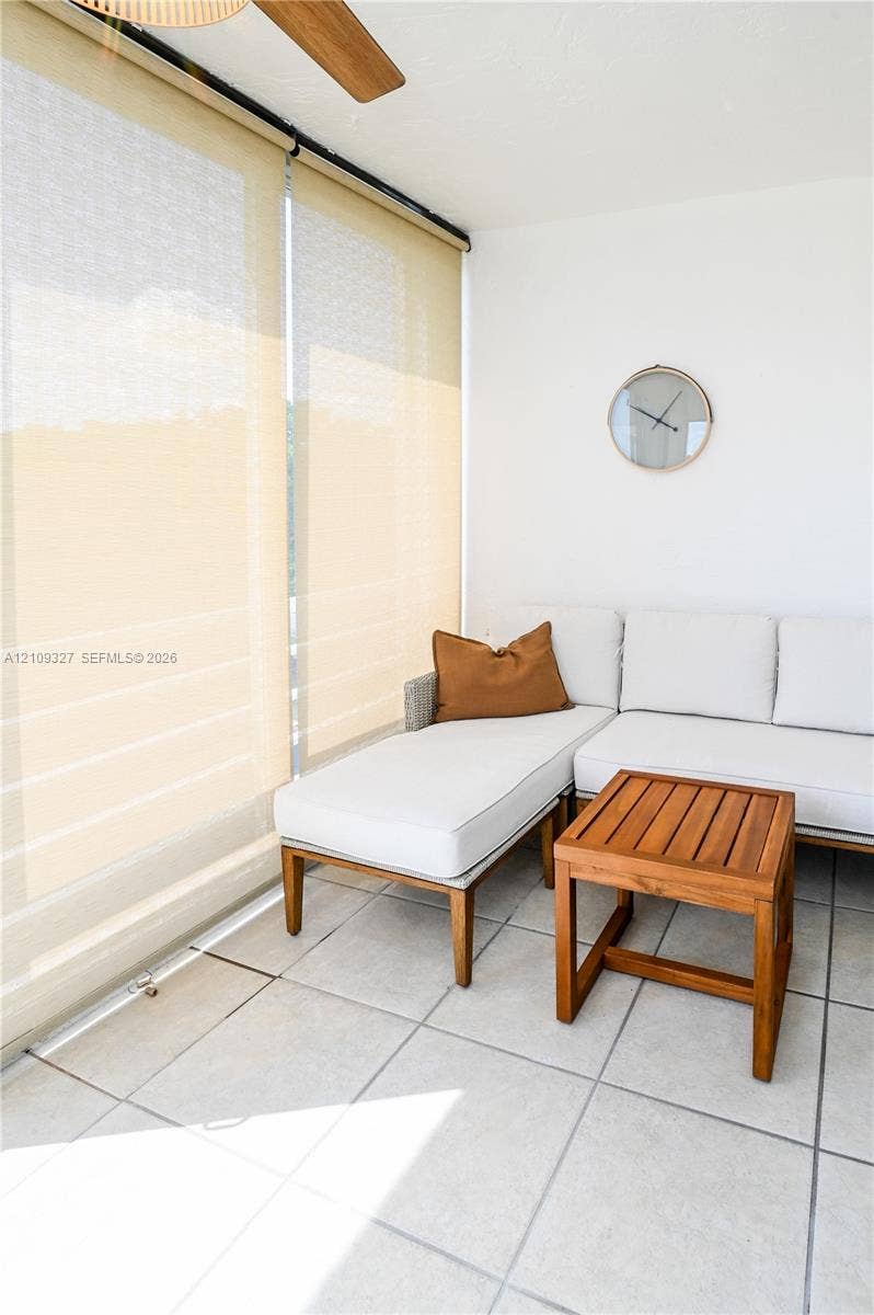 Enclosed space featuring large-format light-toned floor tiling, ceiling-mounted paddle fan, and floor-to-ceiling window shades