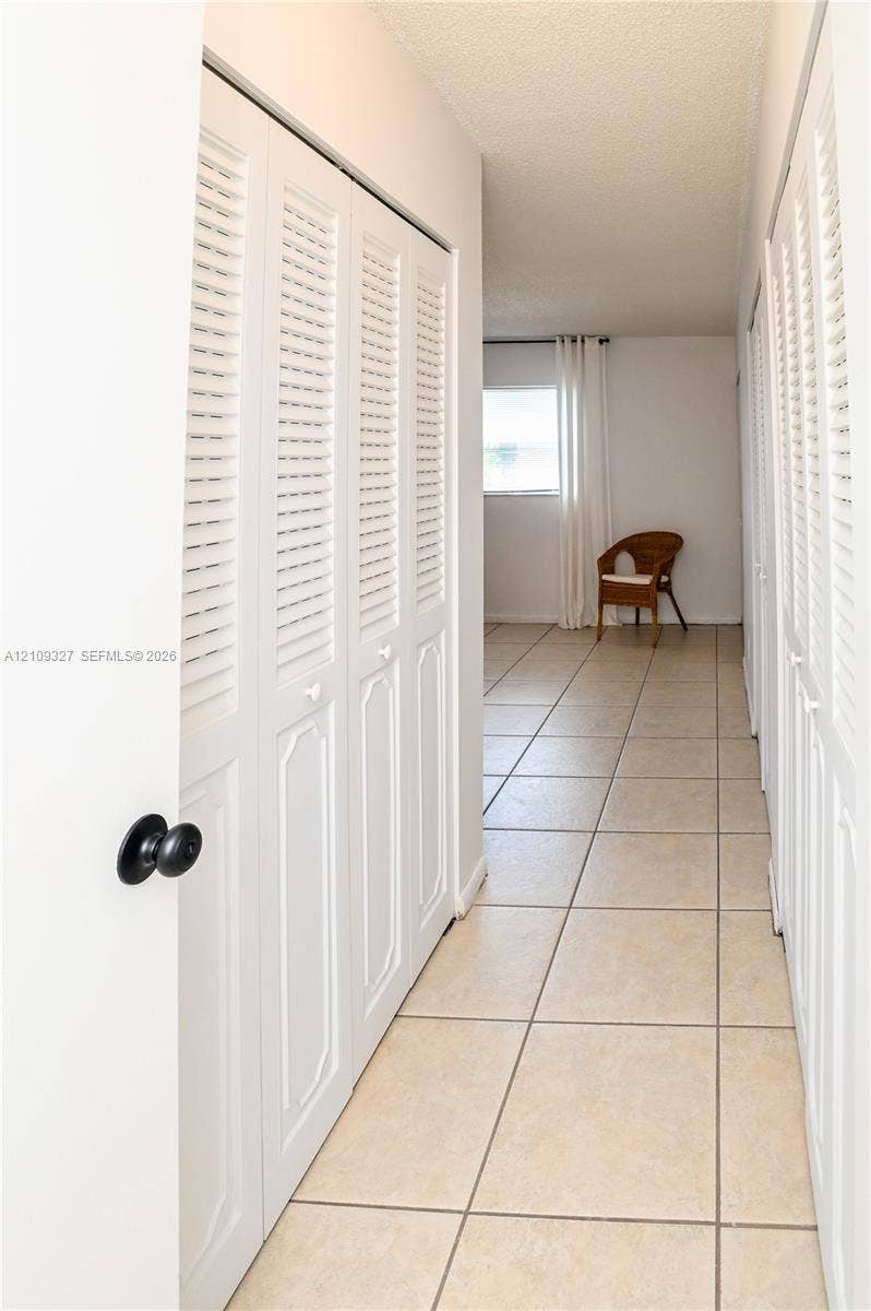 Hallway featuring ceramic tile flooring and multiple sets of white louvered-style closet doors