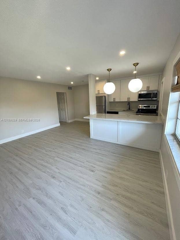 2418 Polk Street, #205, Hollywood, Hollywood, FL 33020 Kitchen featuring white cabinetry, a breakfast bar with stone-finish countertop, recessed lighting, and dual globe pendant lights, complemented by wood-finish flooring