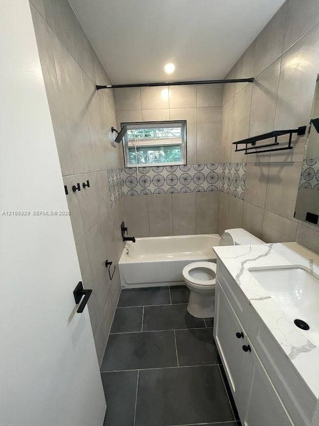 2418 Polk Street, #205, Hollywood, Hollywood, FL 33020 Bathroom featuring a white vanity with a quartz-style countertop, large-format tile flooring, a shower-tub combination with patterned accent tiling, and matte black fixtures