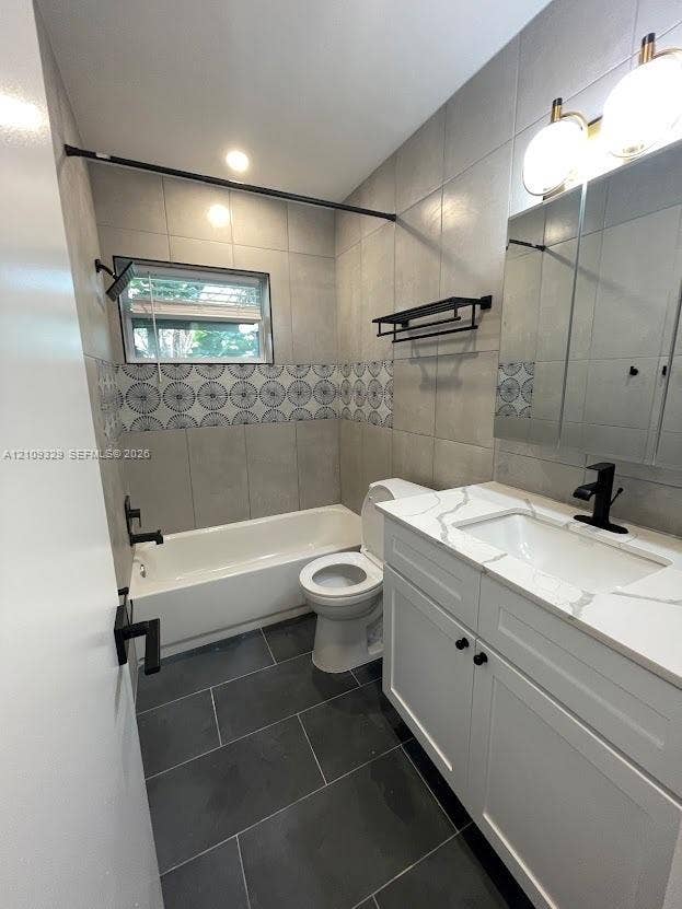 2418 Polk Street, #205, Hollywood, Hollywood, FL 33020 Bathroom featuring a stone-surface vanity with a rectangular sink, matte black fixtures, large-format grey tile flooring, patterned decorative wall tile, and a built-in medicine cabinet