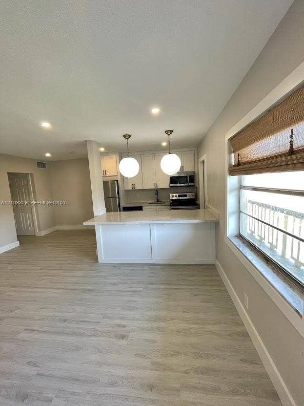 2418 Polk Street, #205, Hollywood, Hollywood, FL 33020 Kitchen featuring a peninsula with white cabinetry, quartz-style countertops, dual globe pendant lighting, and stainless steel appliances, set against wood-finish flooring