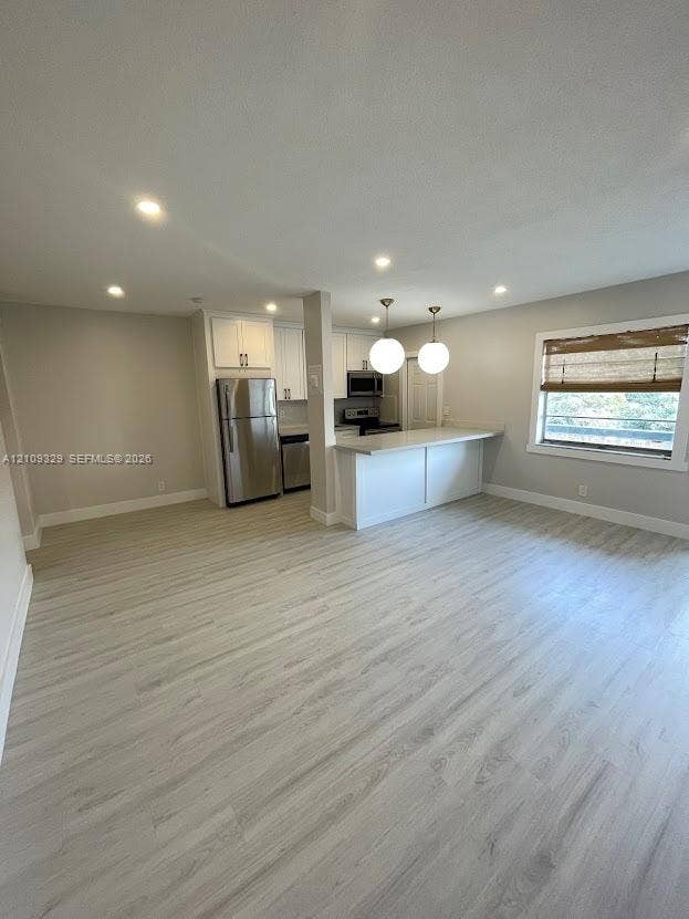 2418 Polk Street, #205, Hollywood, Hollywood, FL 33020 Kitchen featuring white cabinetry, wood-finish flooring, stainless steel appliances, a breakfast bar, and pendant lighting