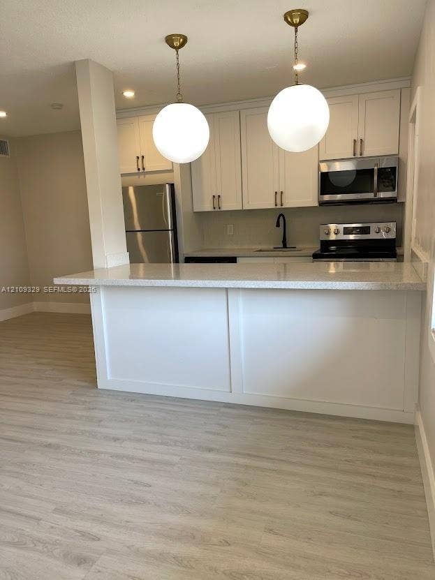 2418 Polk Street, #205, Hollywood, Hollywood, FL 33020 Kitchen featuring white cabinetry, a stone-composite countertop, wood-finish flooring, stainless steel appliances, and dual globe pendant lighting