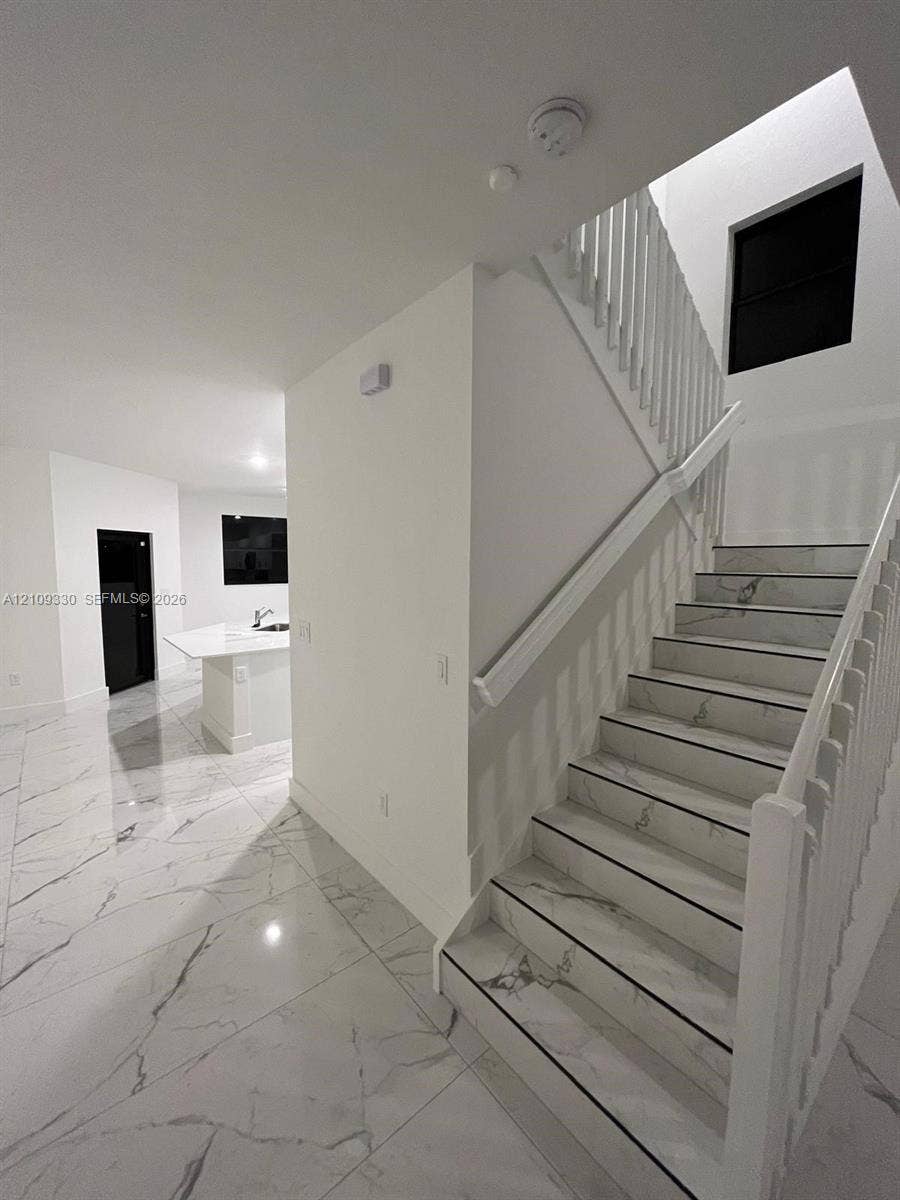 Staircase featuring white balusters and stone-finish treads, complemented by extensive stone-finish floor tiling and a kitchen island with a stone-finish countertop