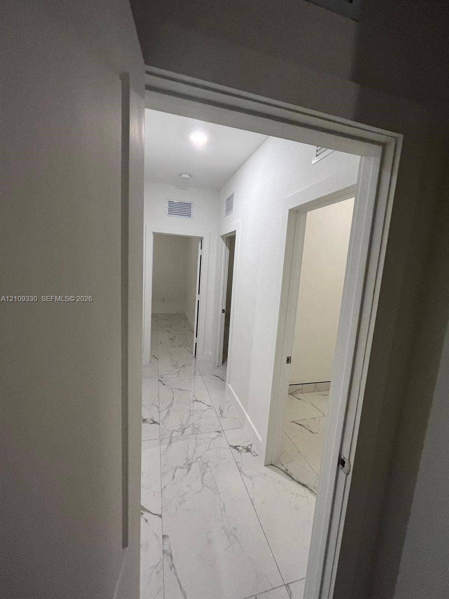 Hallway featuring large-format tile flooring with veining detail, recessed lighting, and white door frames