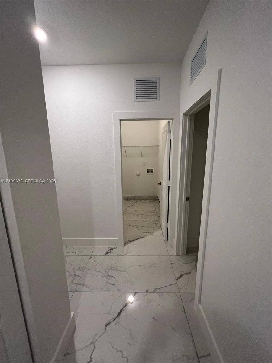 Large-format rectified tile flooring with a veined pattern, neutral wall palette, and walk-in storage area featuring wire shelving