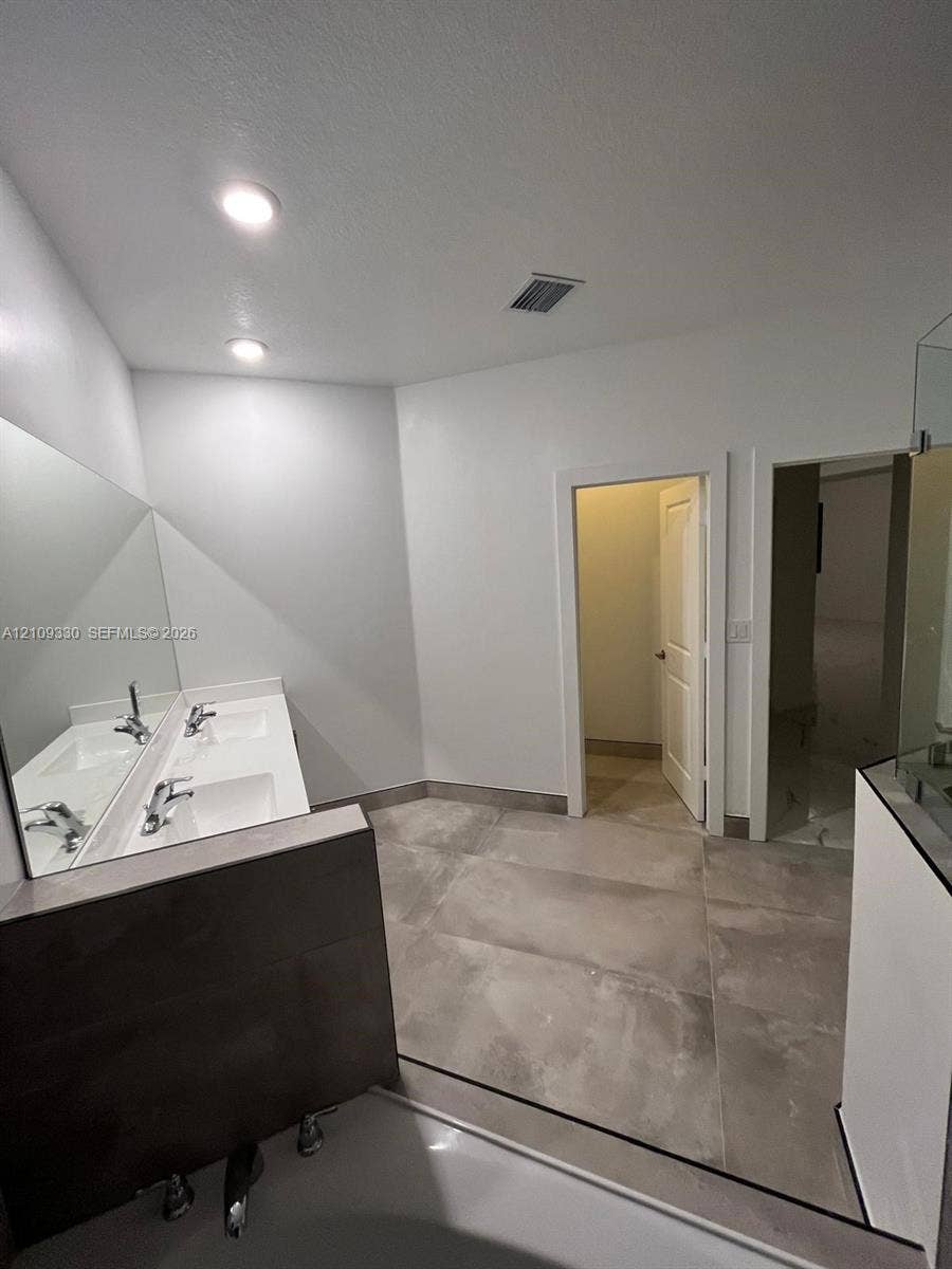 Dual-sink vanity with a large wall-mounted mirror, recessed ceiling lighting, and expansive floor tiling