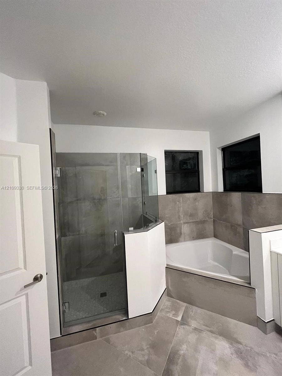 Bathroom featuring a glass-enclosed shower, built-in soaking tub, large-format tile surround, and matte-finish floor tile