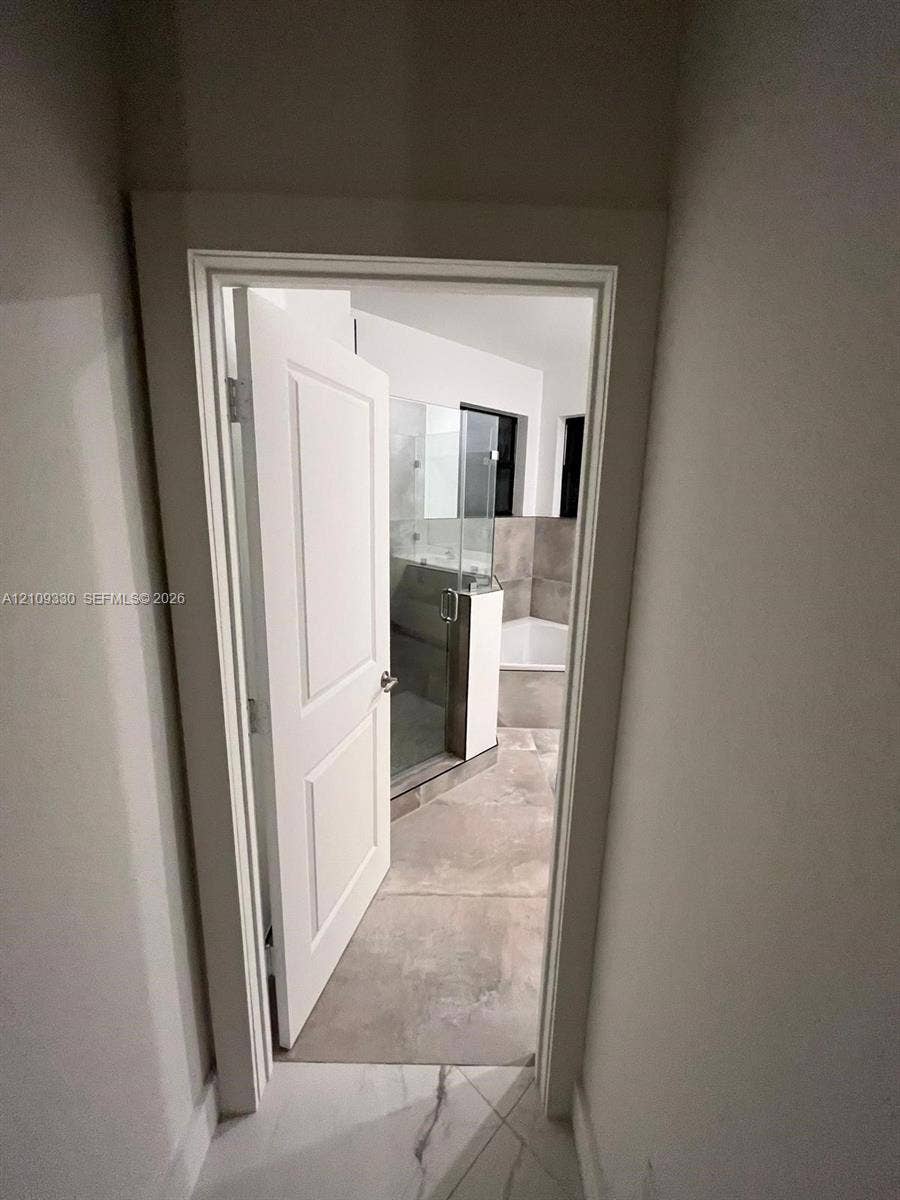 Bathroom interior featuring large-format tile flooring, a glass-enclosed shower, a soaking tub, and a multi-panel door