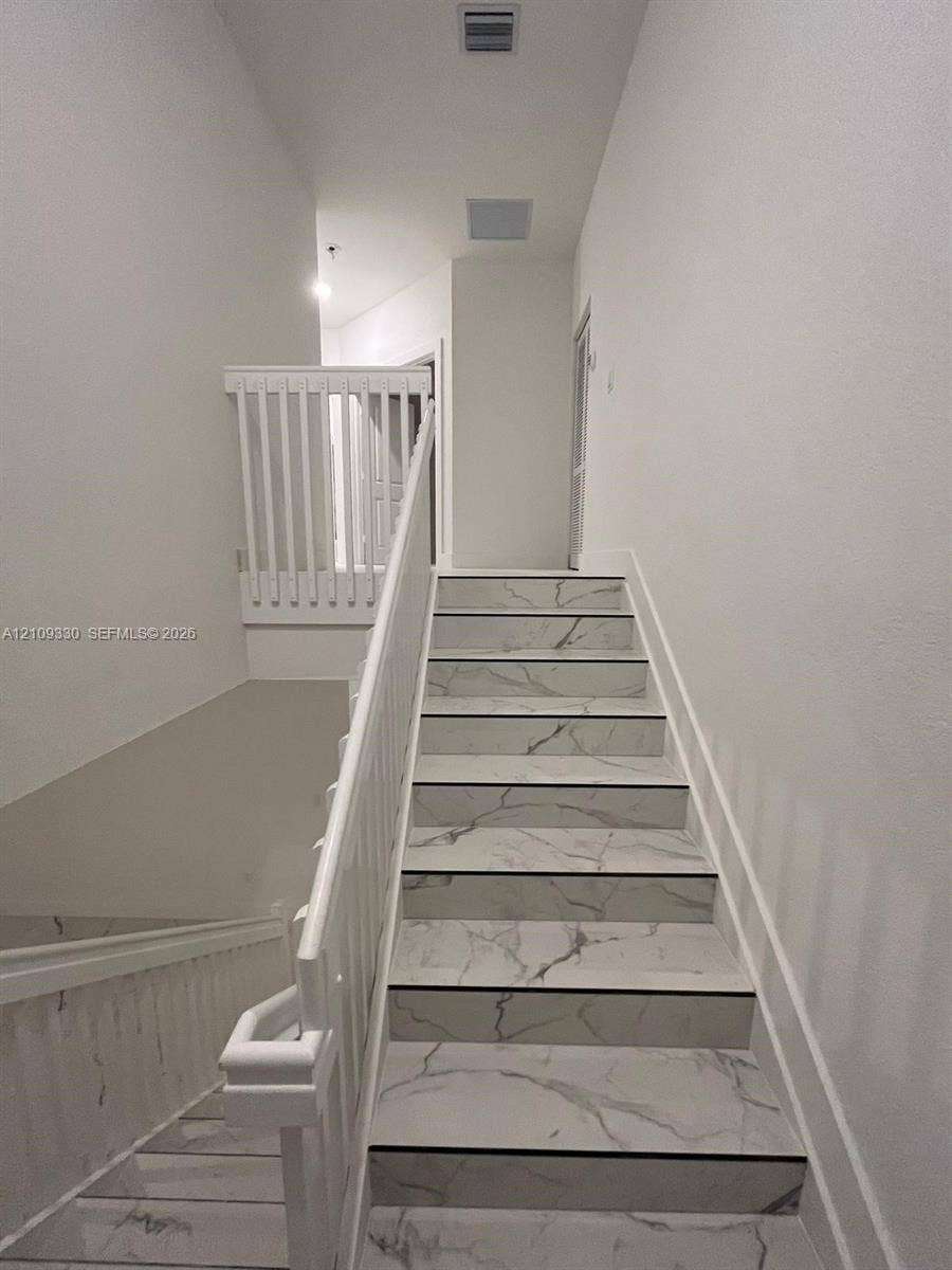 Staircase featuring white stone-patterned treads, white railing, and white balusters