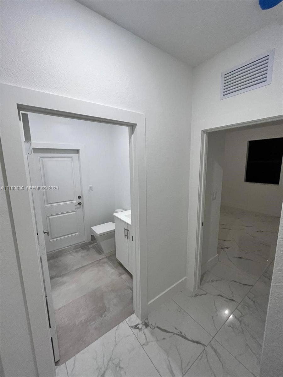 Large-format stone-style tile flooring with neutral veining, white shaker-style cabinetry, and solid-core interior doors