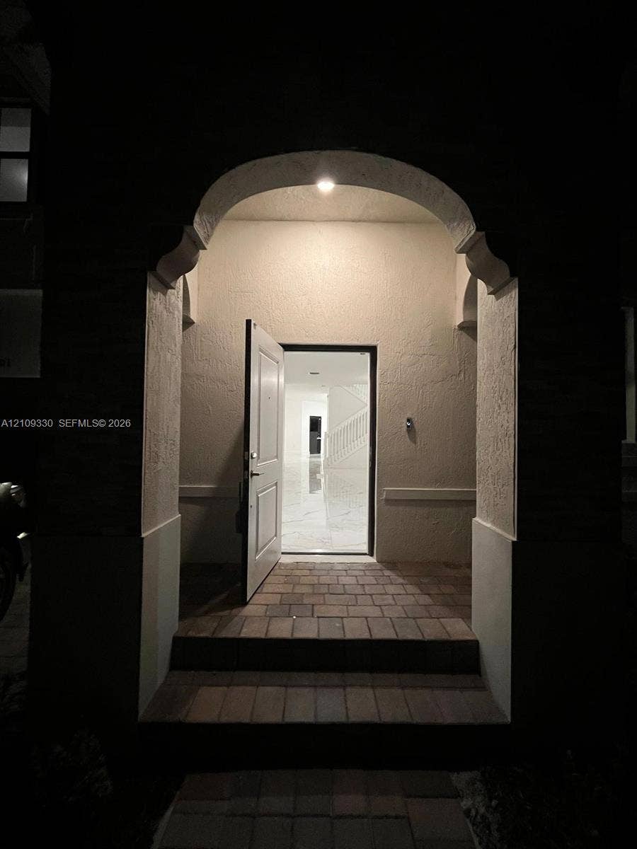 Covered entryway featuring a stone-paver stoop and an arched architectural opening with recessed lighting