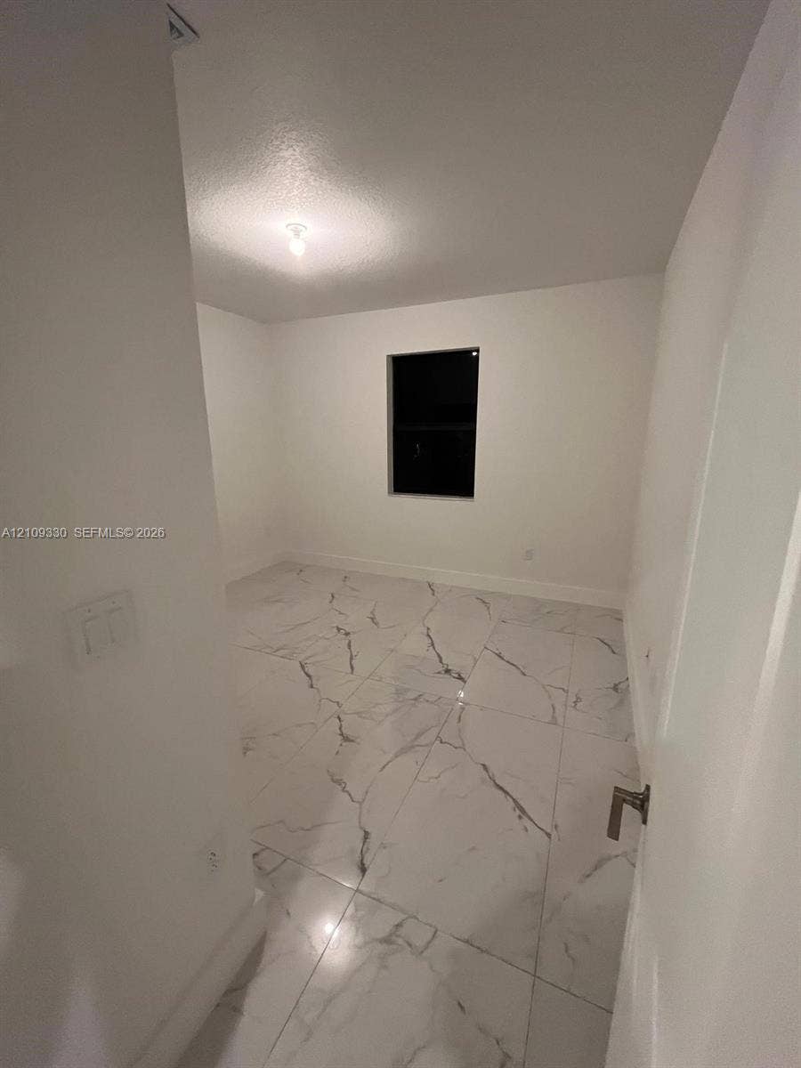 Interior space featuring large-format white stone-finish flooring with dark veining, neutral wall paint, and a single-pane window