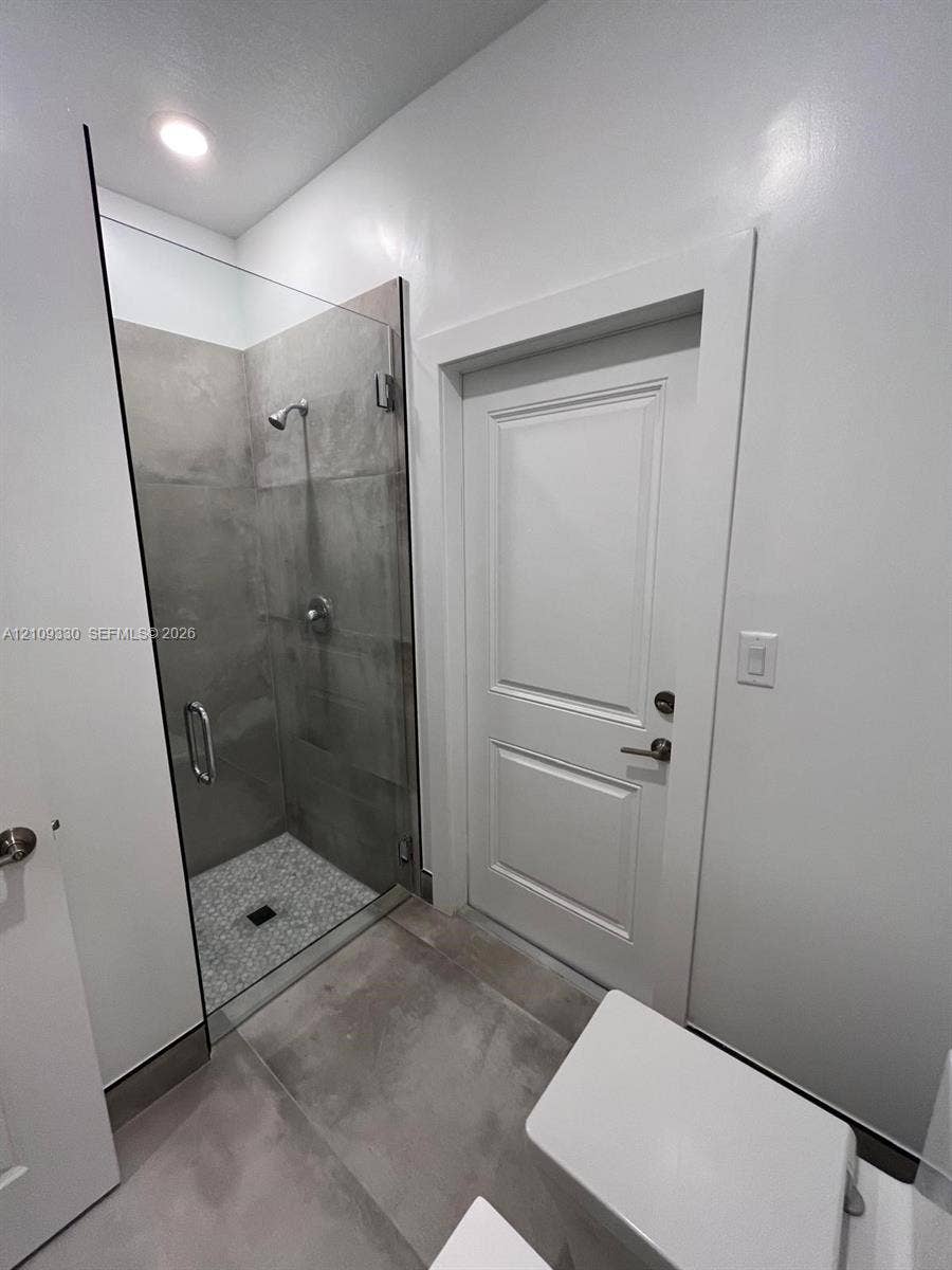 Walk-in shower featuring a frameless glass door, large-format grey tile surround, mosaic stone-finish floor, and metallic hardware