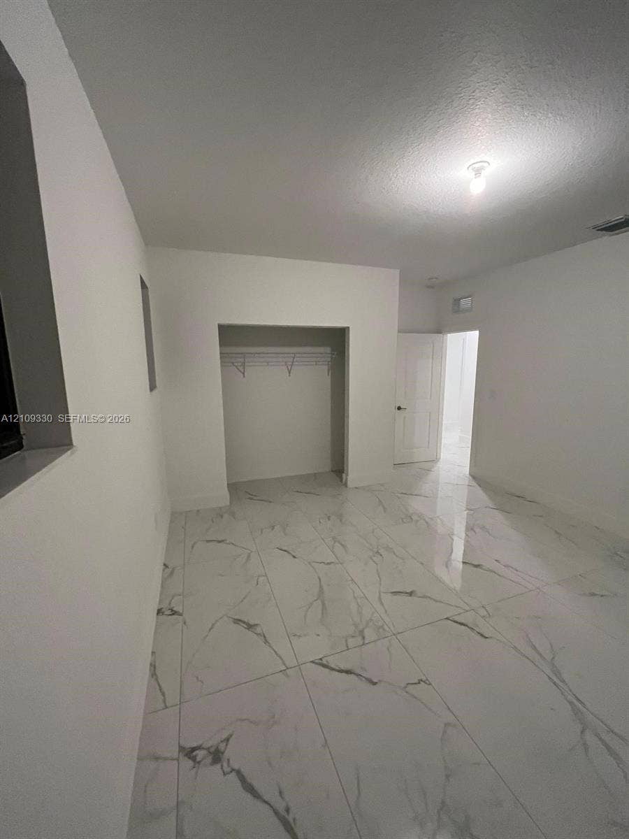 Neutral-toned room featuring large-format polished tile flooring with marble-style veining, recessed closet area, and crisp white wall finishes