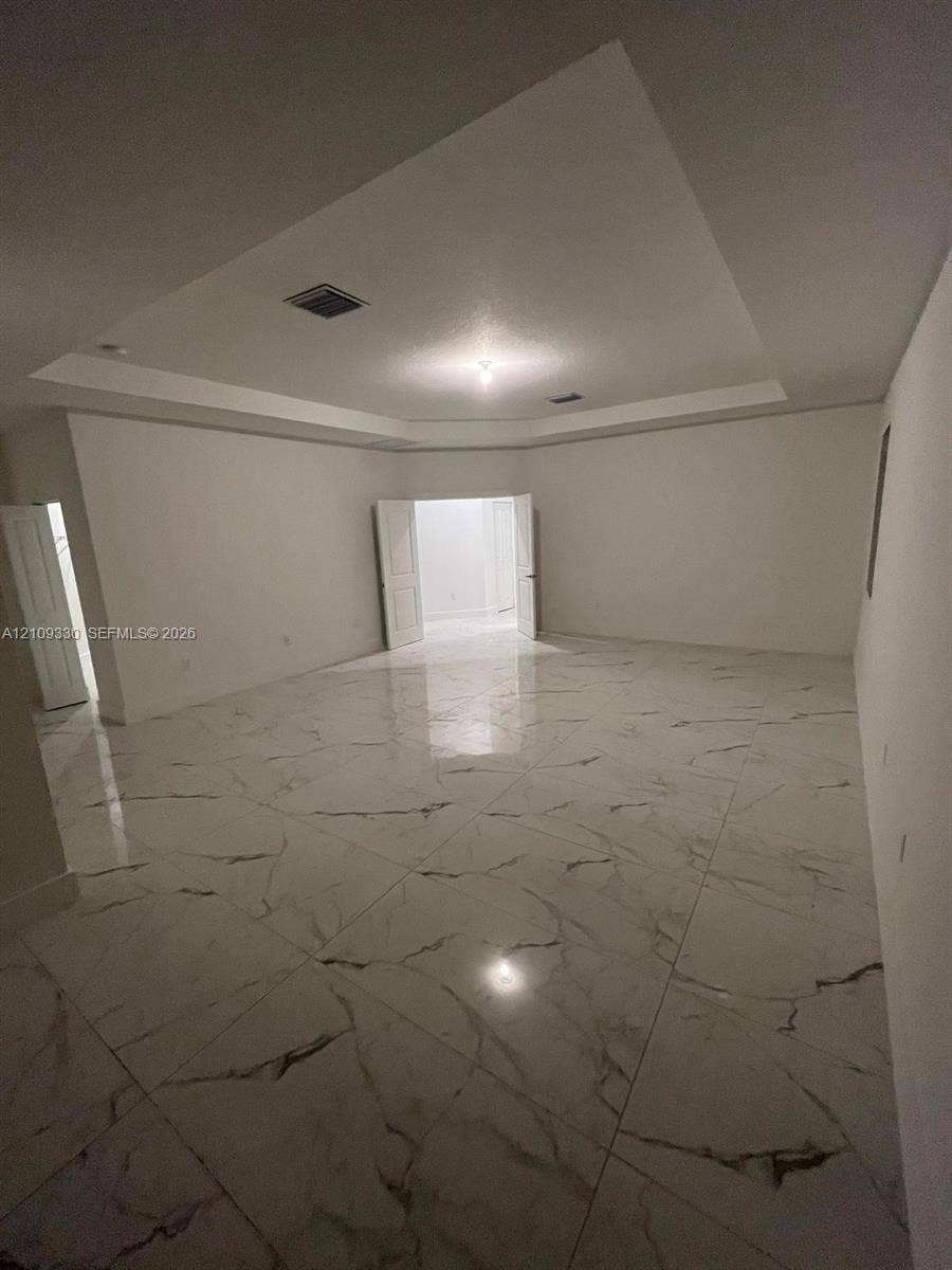 Tray ceiling, large-format stone-finish flooring with neutral veining, and double-door entry