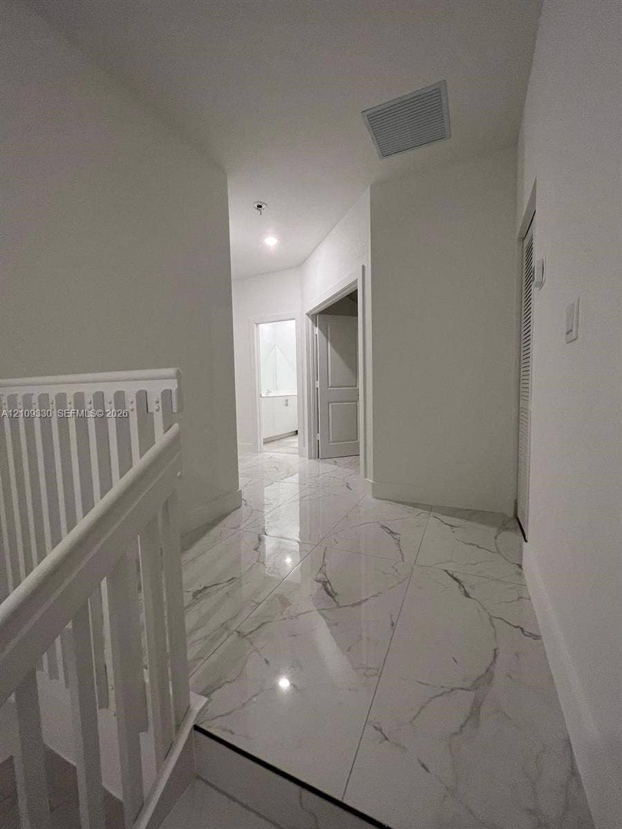 Large-format tile flooring with a veined pattern, white painted walls, and white wooden stair railing with vertical balusters