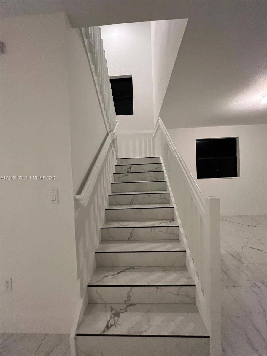 Staircase featuring white stone-finish treads with grey veining, a painted white handrail, and white balusters