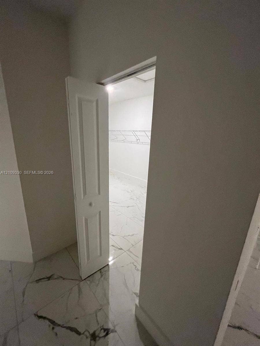 Storage space featuring white, six-panel bi-fold doors, white wire shelving, and large-format tile flooring with marble-pattern veining