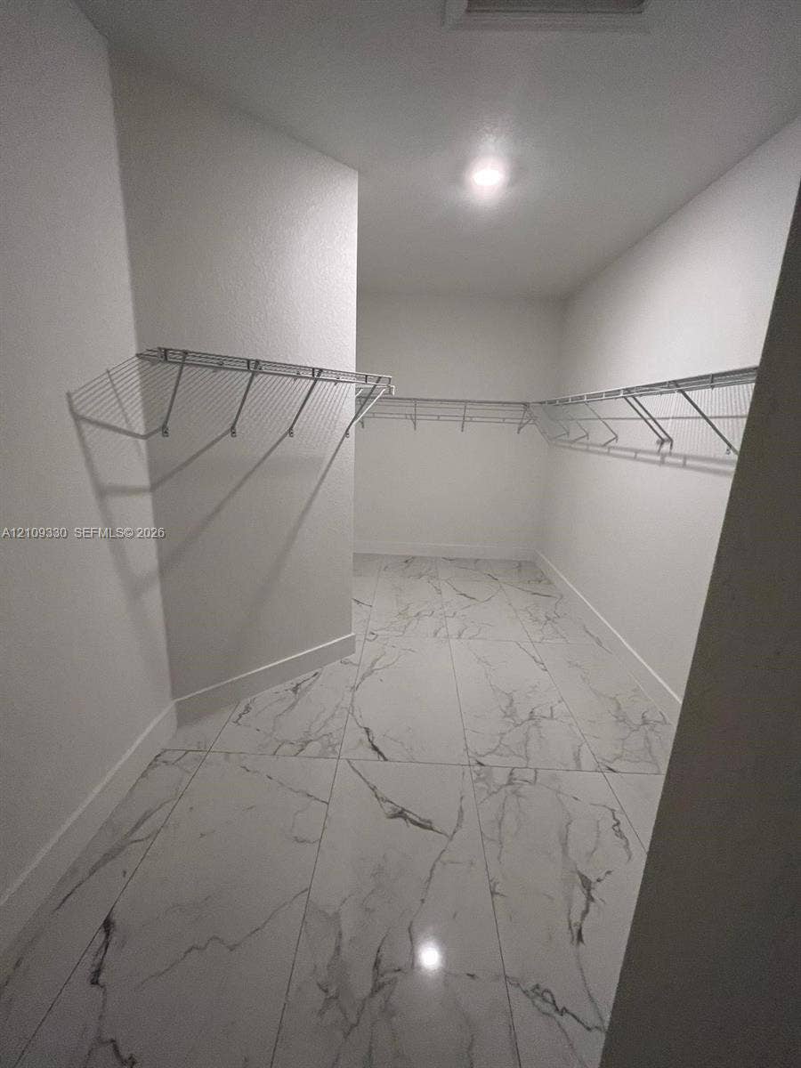 Walk-in closet featuring large-format tile flooring with a neutral veined pattern, white walls, and tiered metal wire shelving