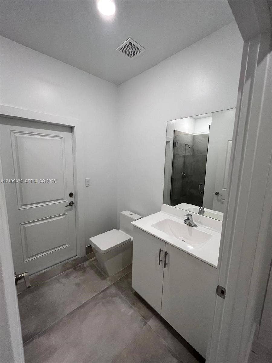 Bathroom featuring a white vanity cabinet with a integrated sink, polished chrome faucet, large frameless mirror, and neutral-toned tiled flooring