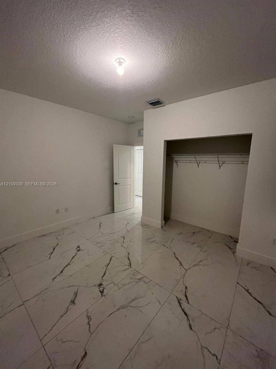 Interior room featuring large-format stone-patterned floor tile, a recessed walk-in closet with integrated shelving, and a paneled interior door