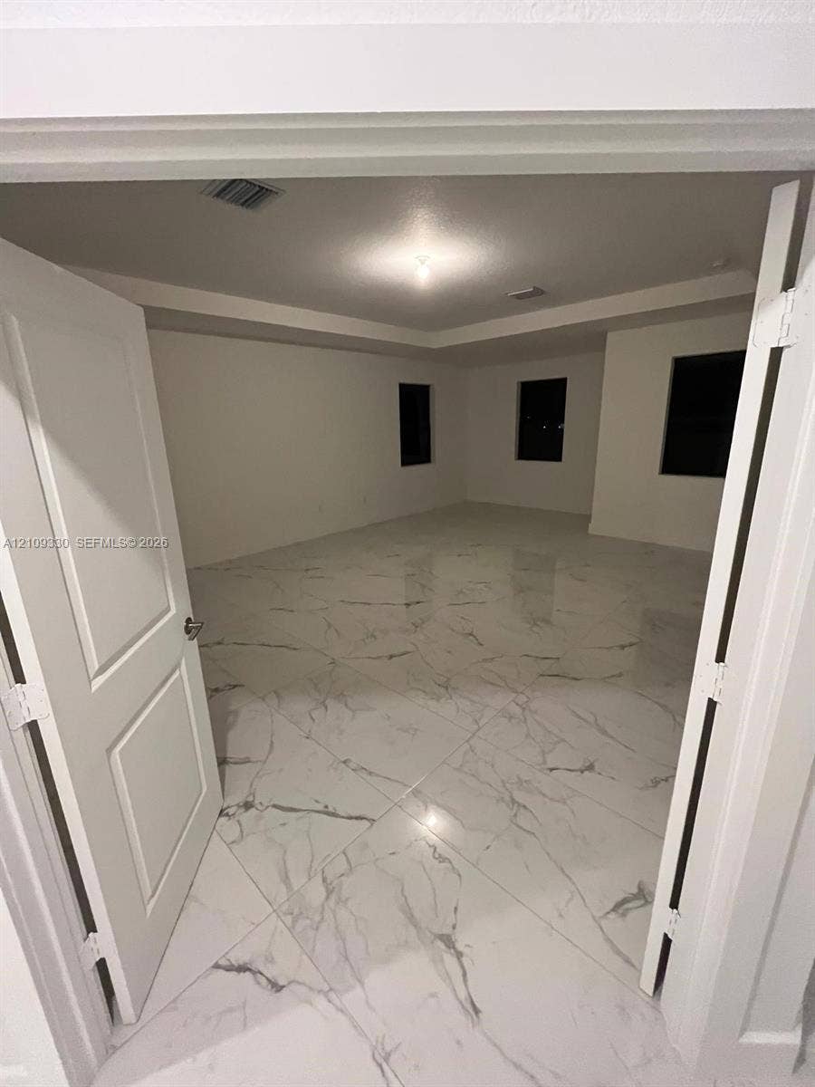 Interior space featuring polished large-format tile flooring with veining, tray ceiling, and double door entry