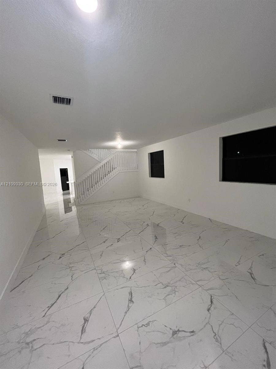 Large-format stone-patterned tile flooring, recessed lighting, and a staircase featuring a white wooden balustrade