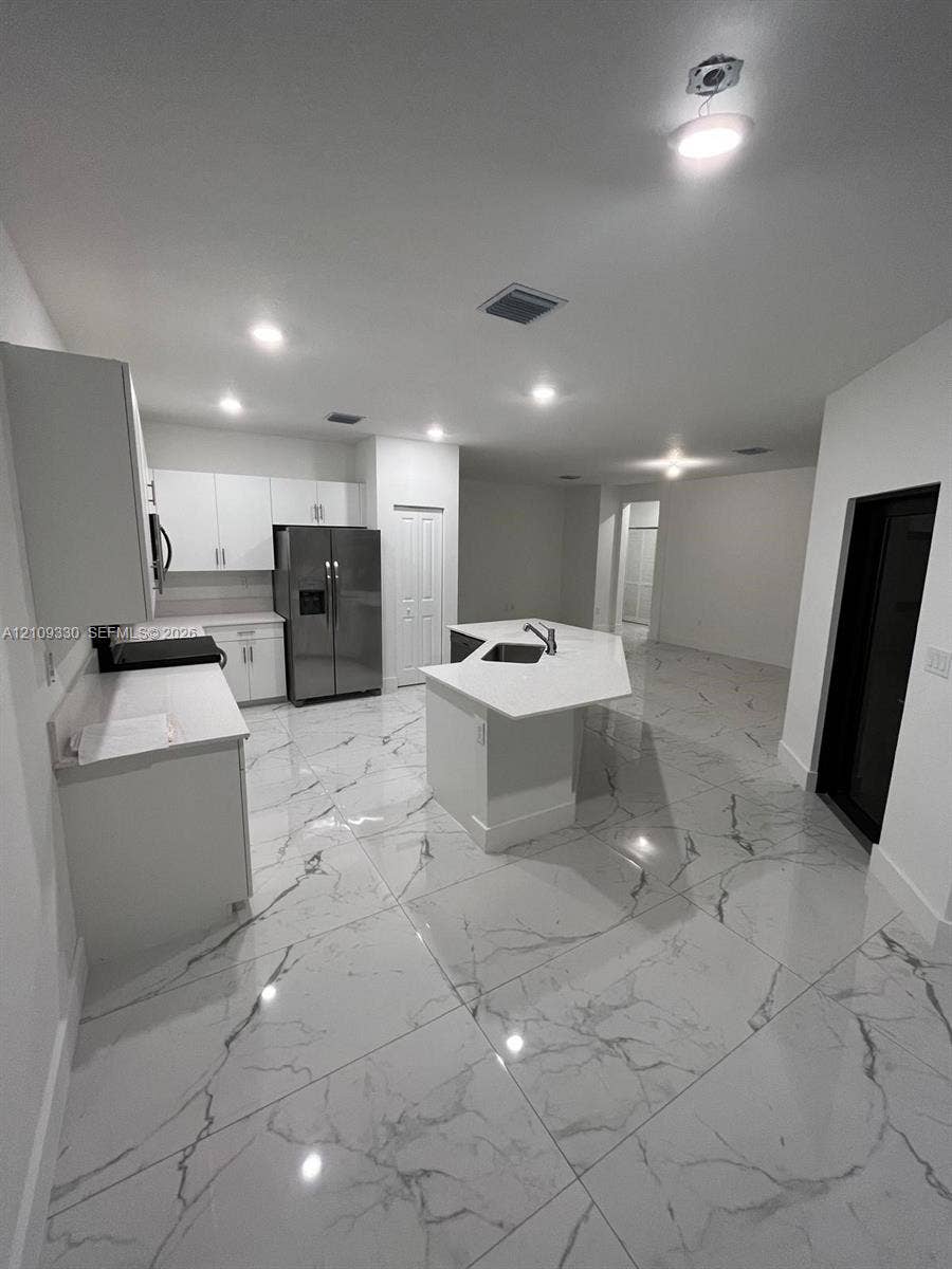 Kitchen featuring white cabinetry, center island with stone-finish countertops, stainless steel appliances, and large-format porcelain tile flooring