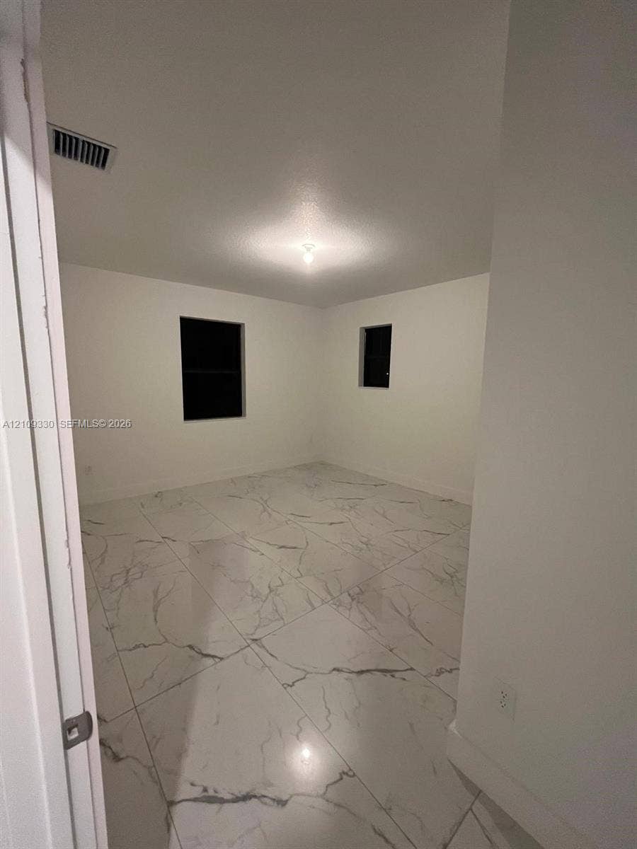 Room featuring large-format white tile flooring with grey veining, neutral wall tones, and two windows
