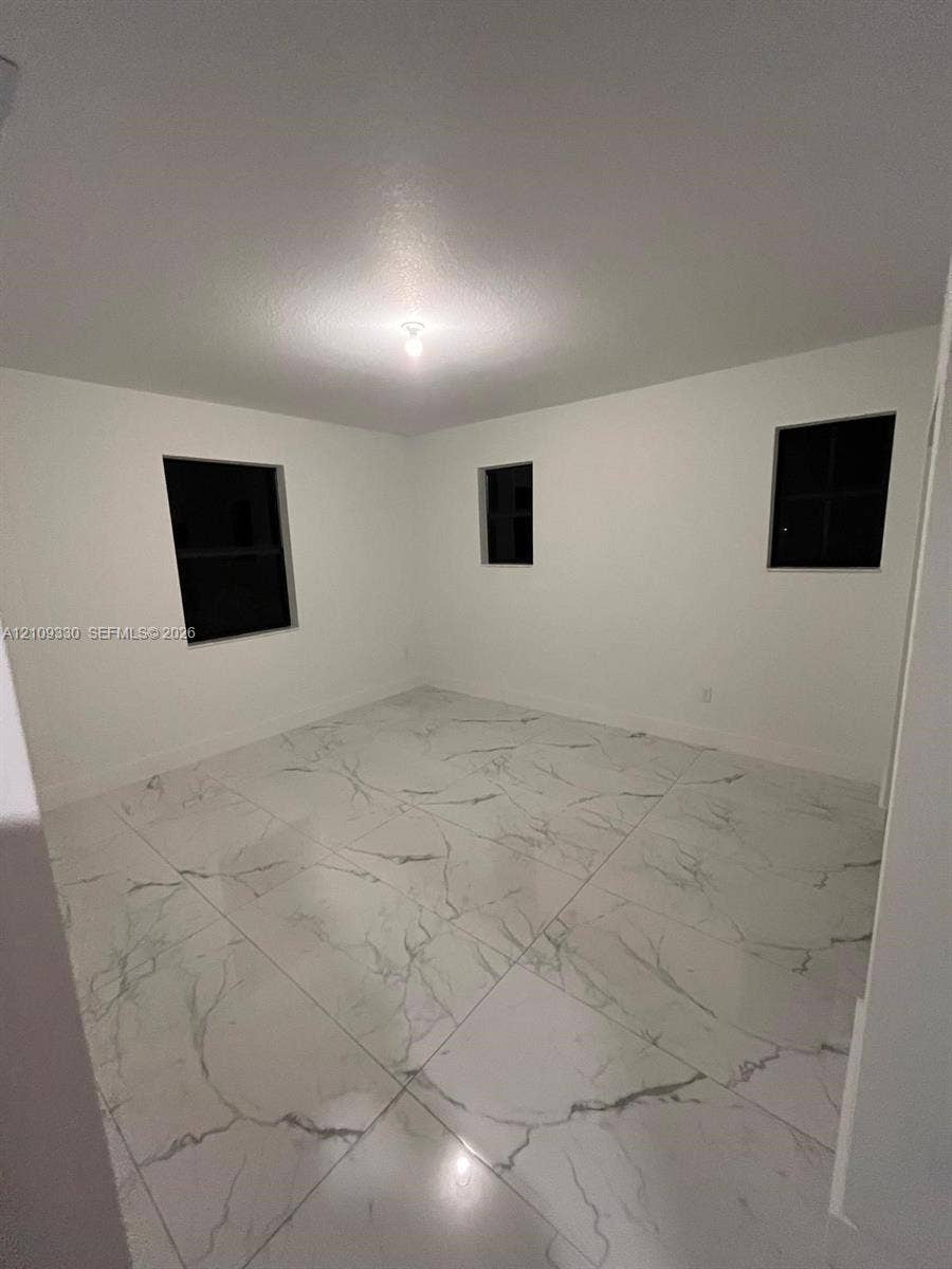 Room featuring large-format white stone-finish flooring with dark grey veining, crisp neutral wall paint, and three windows